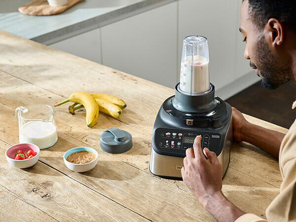 Eine Person benutzt einen Mixer mit verschiedenen Zutaten auf einem Holztisch.