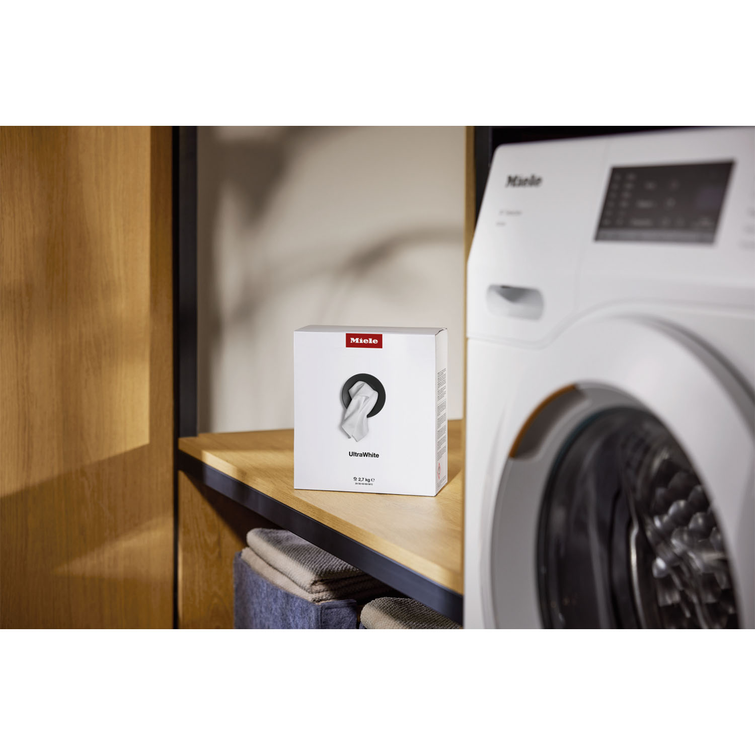 Una scatola bianca di detersivo Miele UltraWhite accanto a una lavatrice bianca.