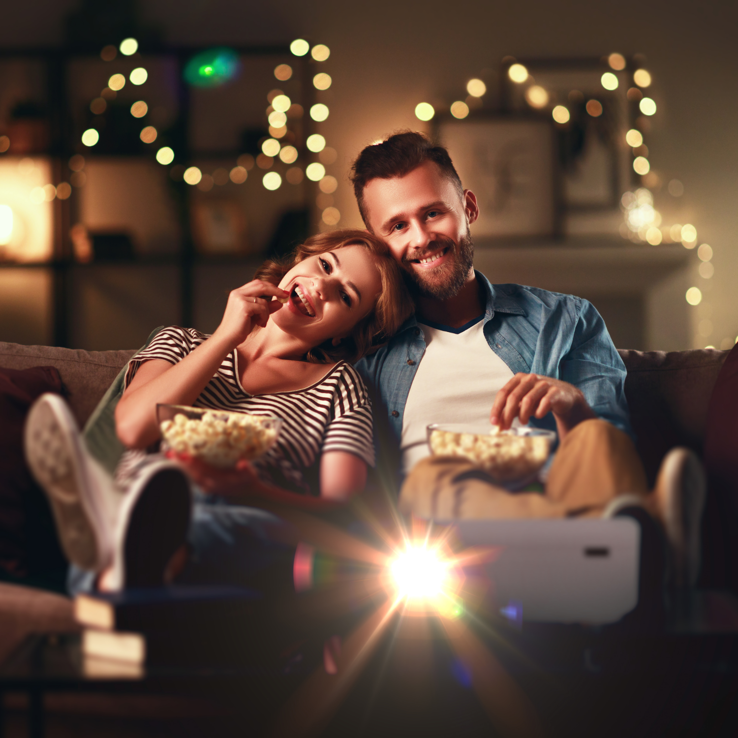 Couple sur un canapé regardant un film, mangeant du pop-corn, avec un projecteur visible.