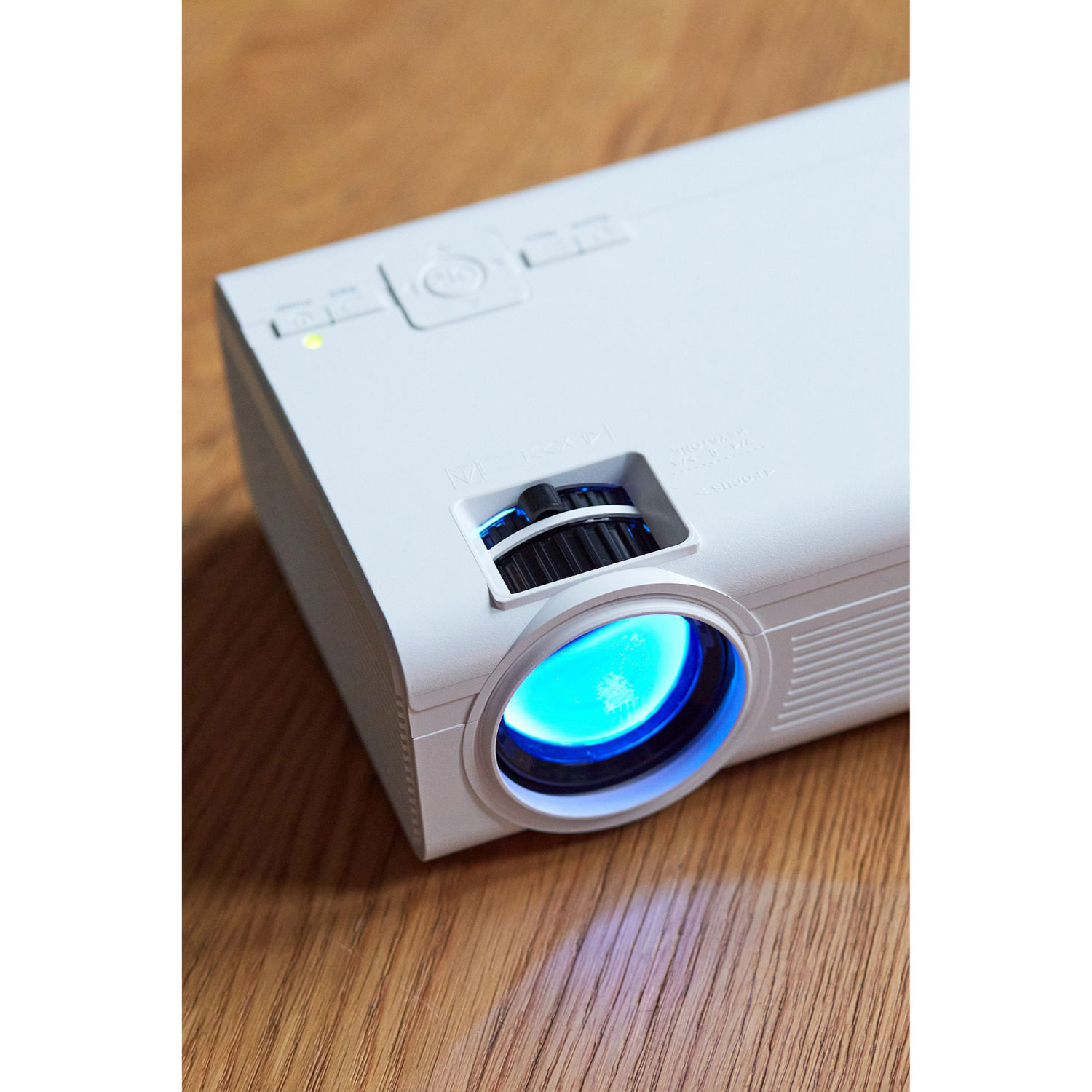 Projecteur blanc avec une lumière bleue émise par la lentille. Fond en bois.
