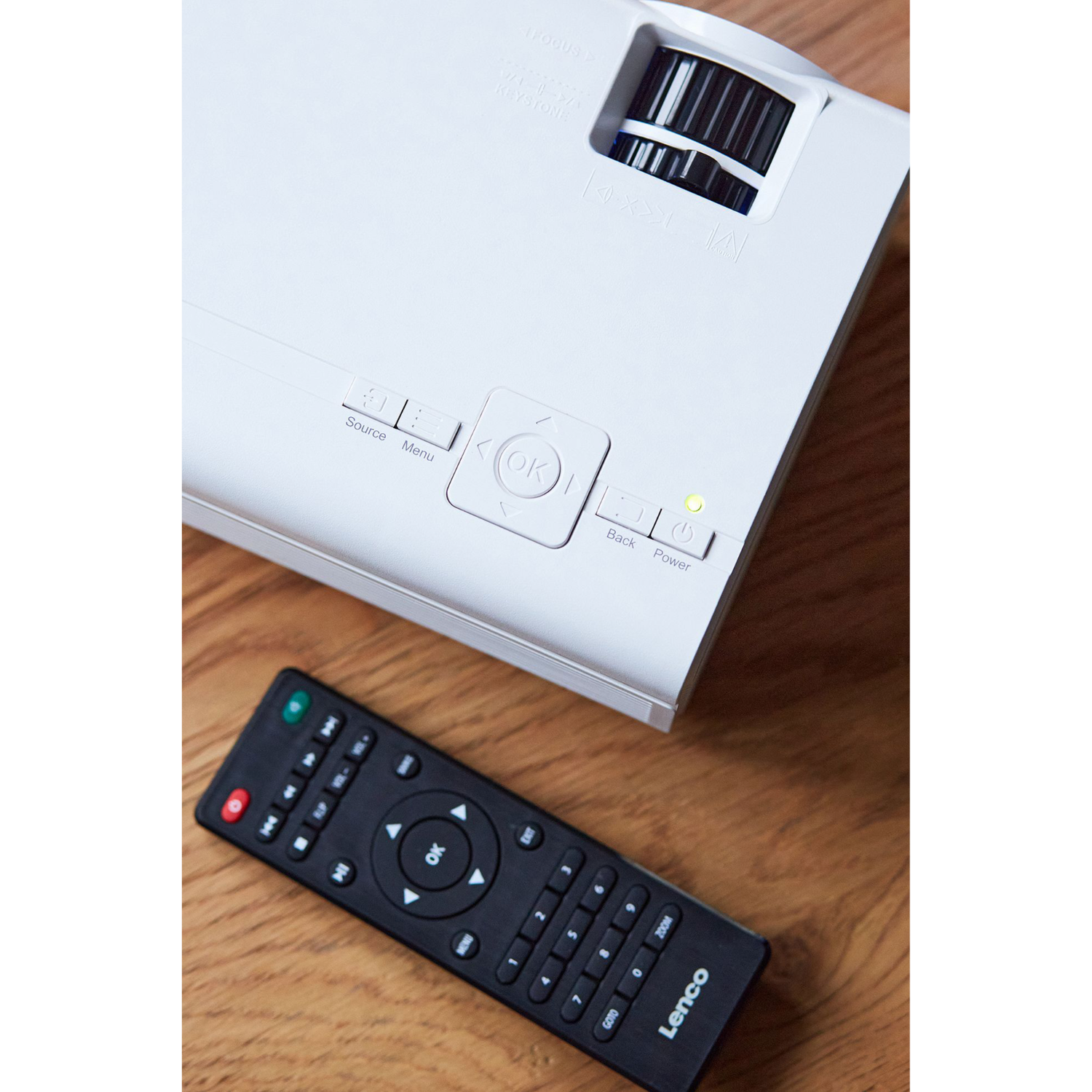 Un projecteur blanc avec boutons et une télécommande sur une table en bois.