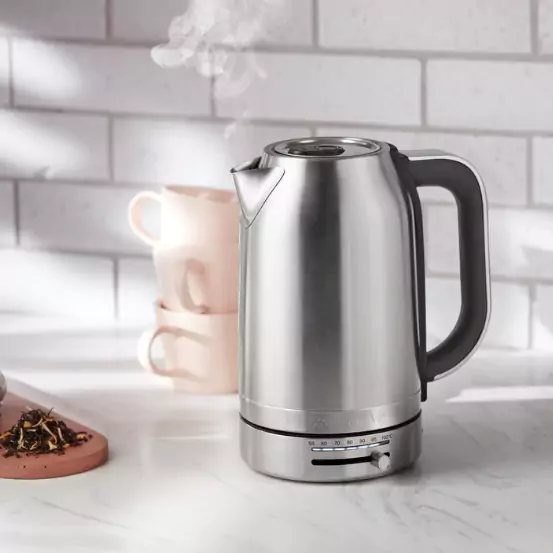 Rozsdamentes acél elektromos vízforraló fehér pulton. Tea és csészék a háttérben.