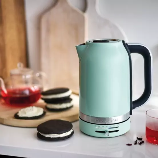 Mentazöld elektromos vízforraló a pulton. Mellette sütik és egy pohár tea.