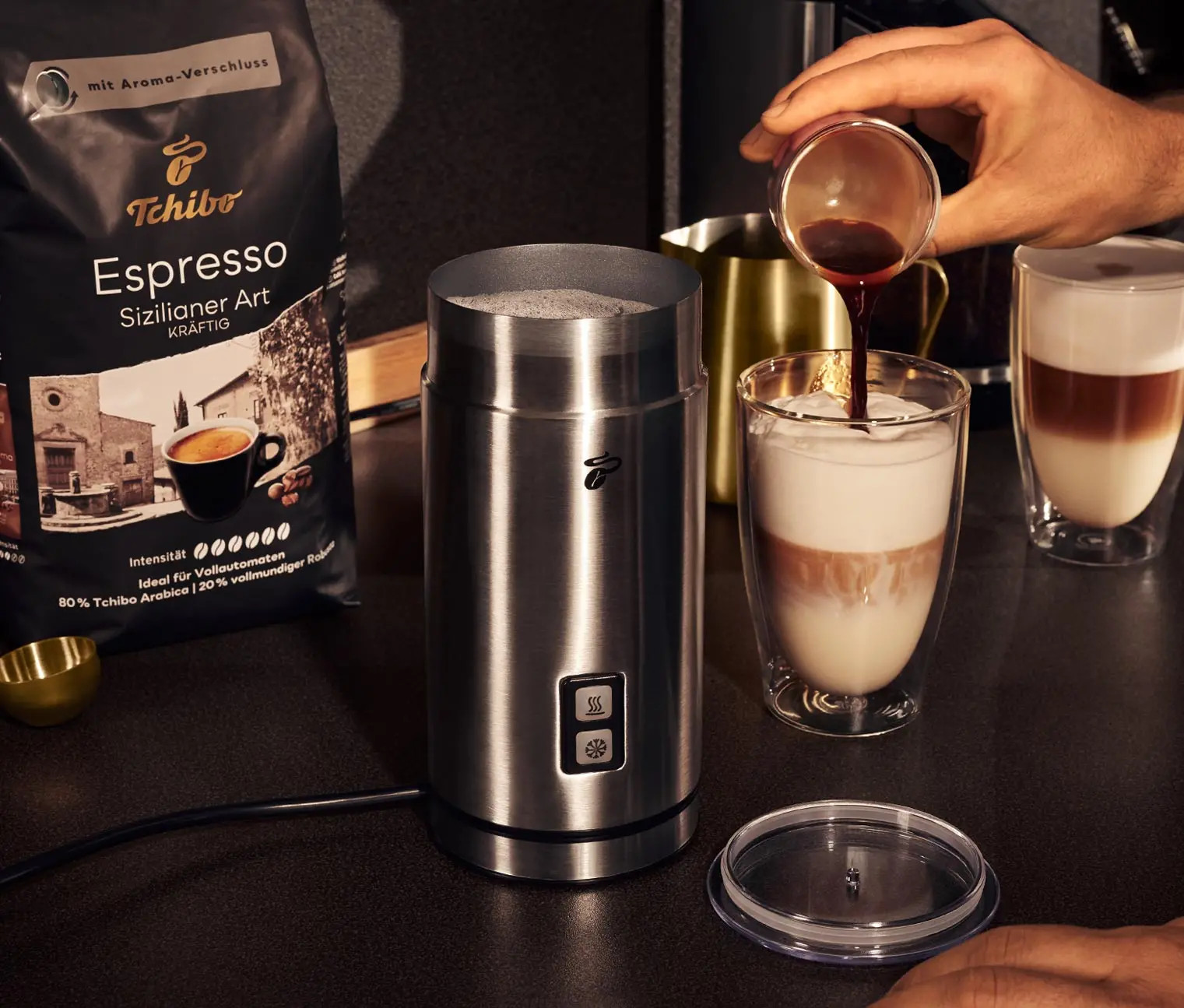 Osoba wlewa kawę do szklanki obok spieniacza.