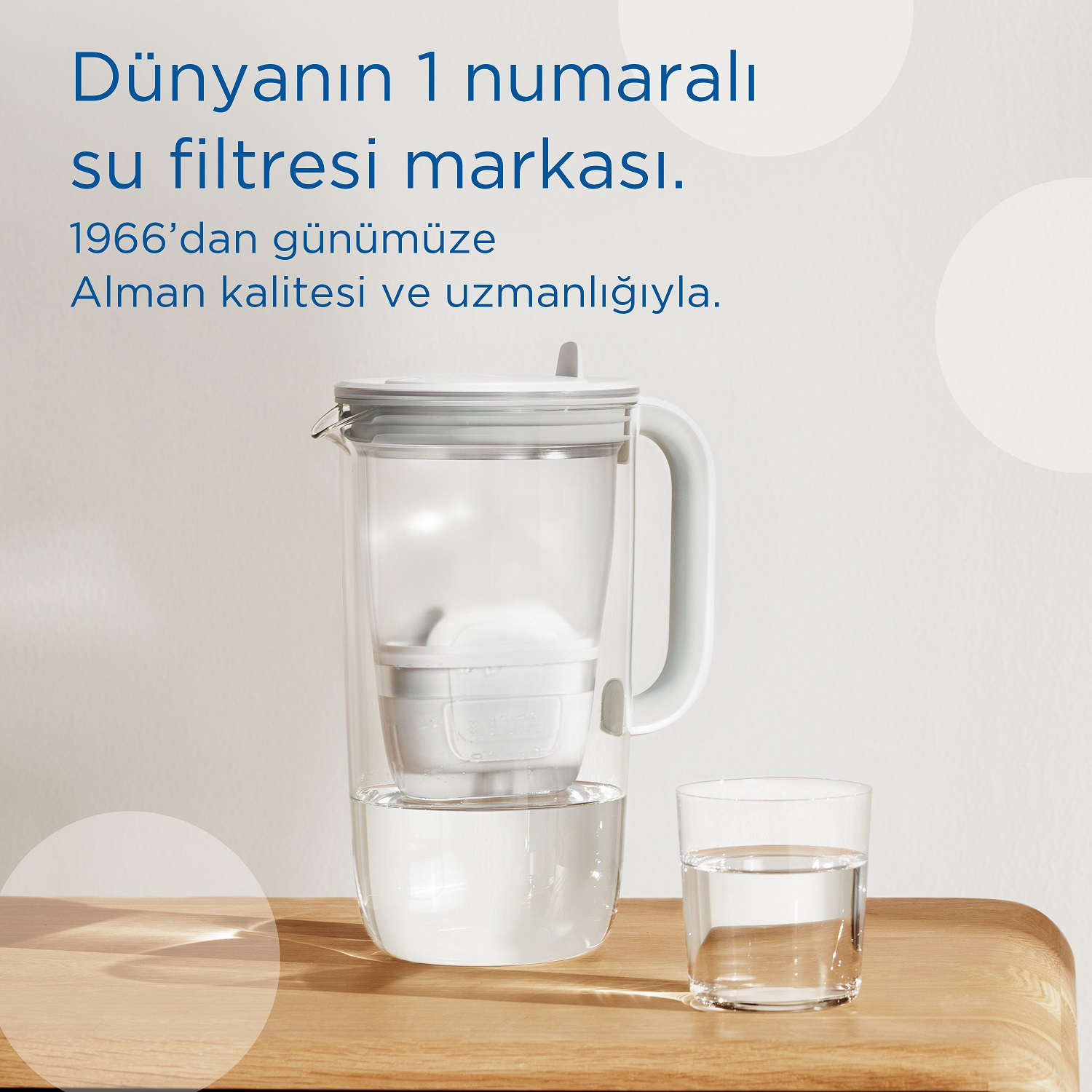 Ahşap bir yüzey üzerinde bir su filtresi sürahisi ve bir bardak su, ürün hakkında Türkçe metinlerle.