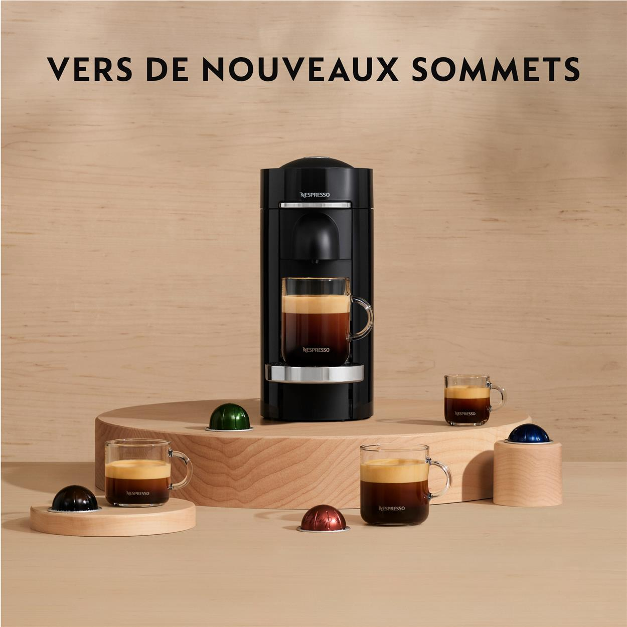Machine à café noire avec tasses en verre et capsules sur plateforme en bois, texte en haut.