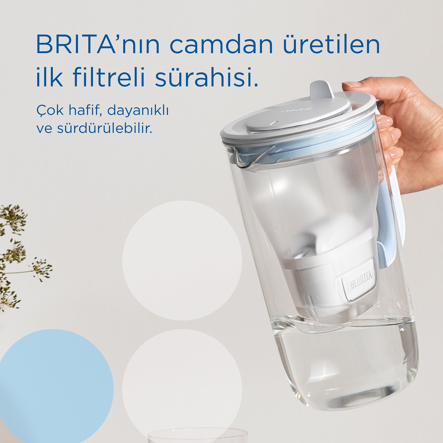 Mavi kapaklı şeffaf su filtresi sürahisi. Sürahiyi tutan el.