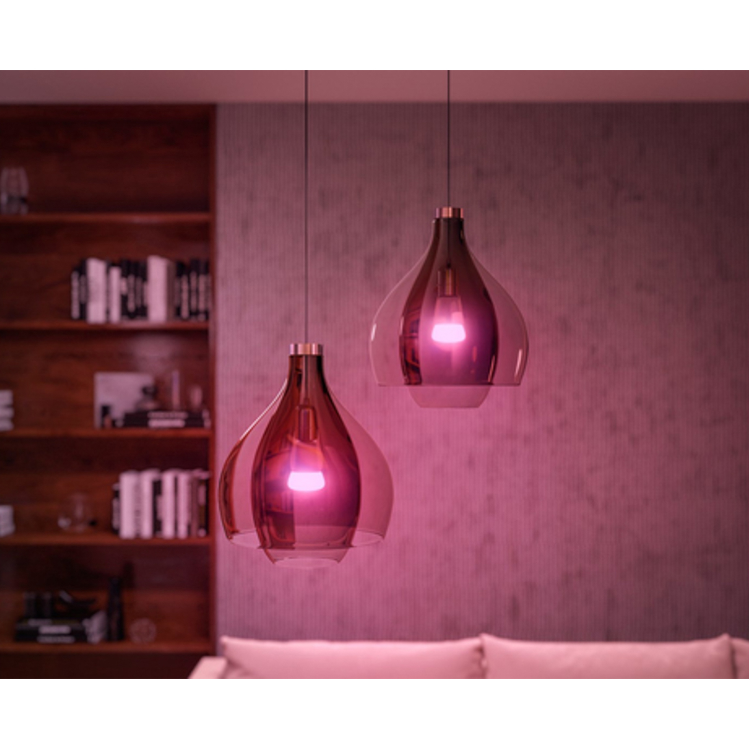 Due lampade a sospensione con bagliore rosa. Le luci sono in vetro e a forma di pera, appese al soffitto.