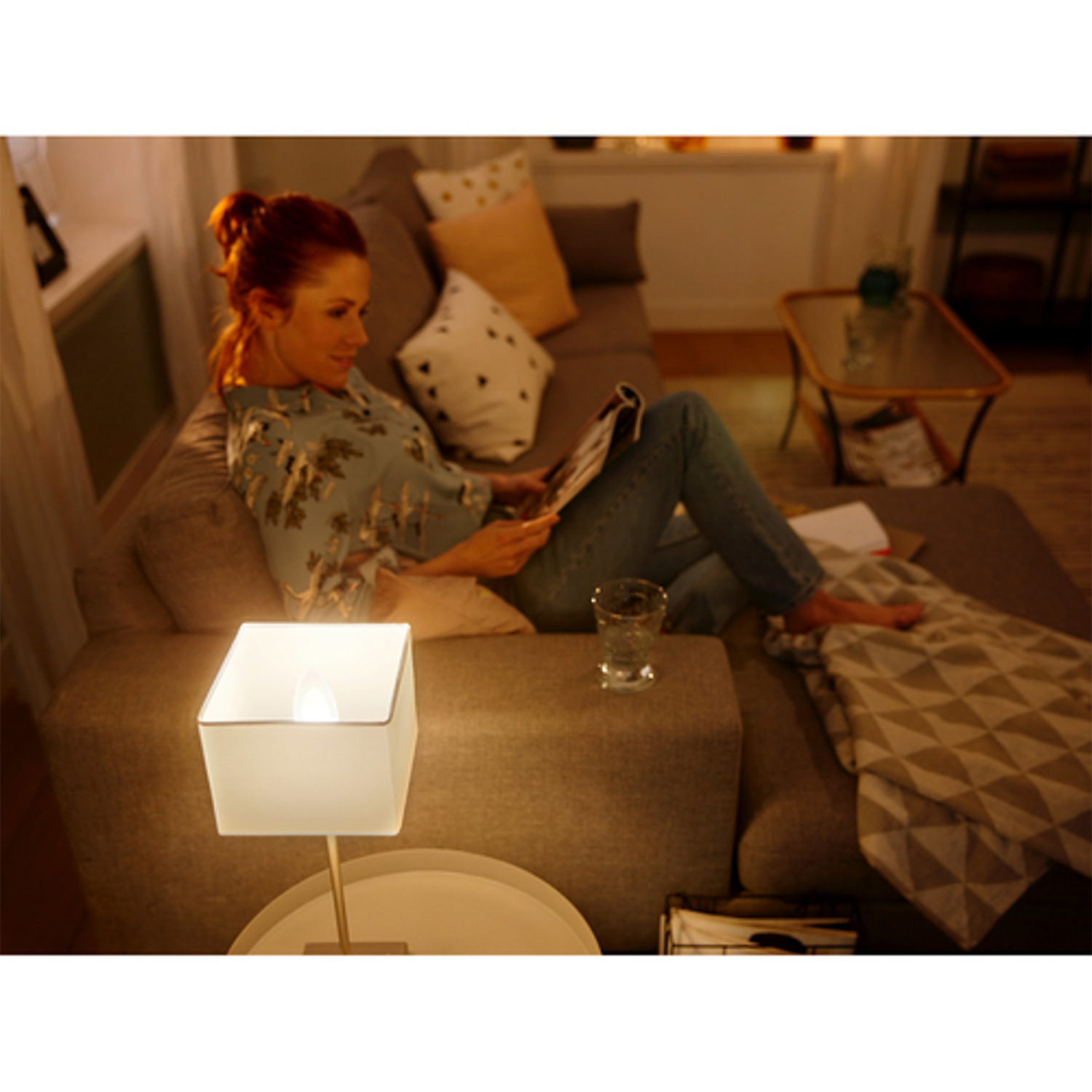 Donna sul divano che legge con una lampada, ambiente domestico accogliente.