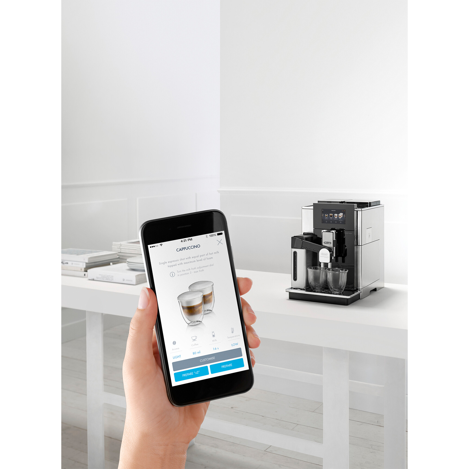 Una mano che tiene un telefono che mostra l'interfaccia di una macchina da caffè accanto alla macchina su un tavolo.
