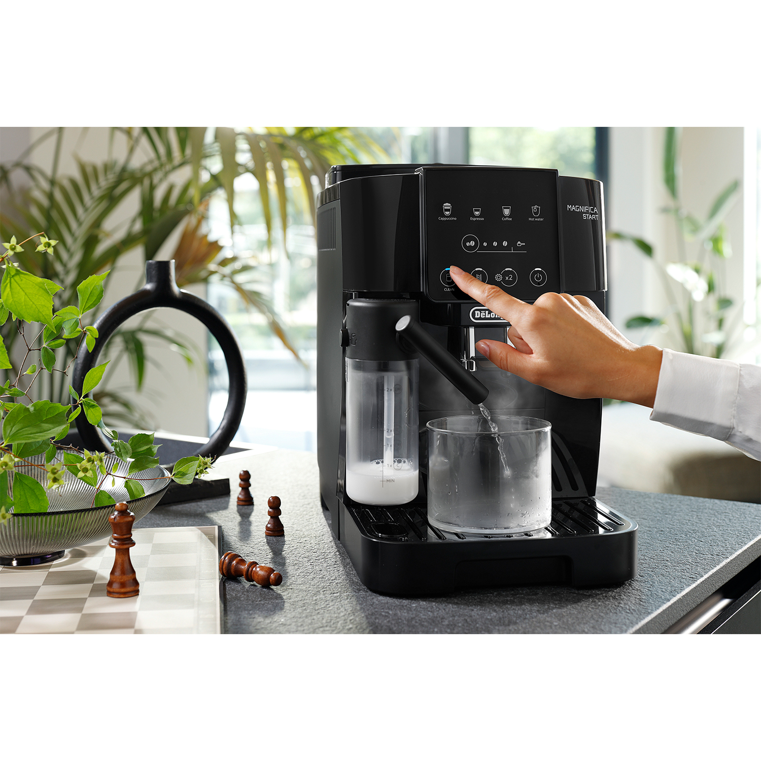 Macchina da caffè DeLonghi Magnifica Evo nera con la mano di una persona che la aziona.