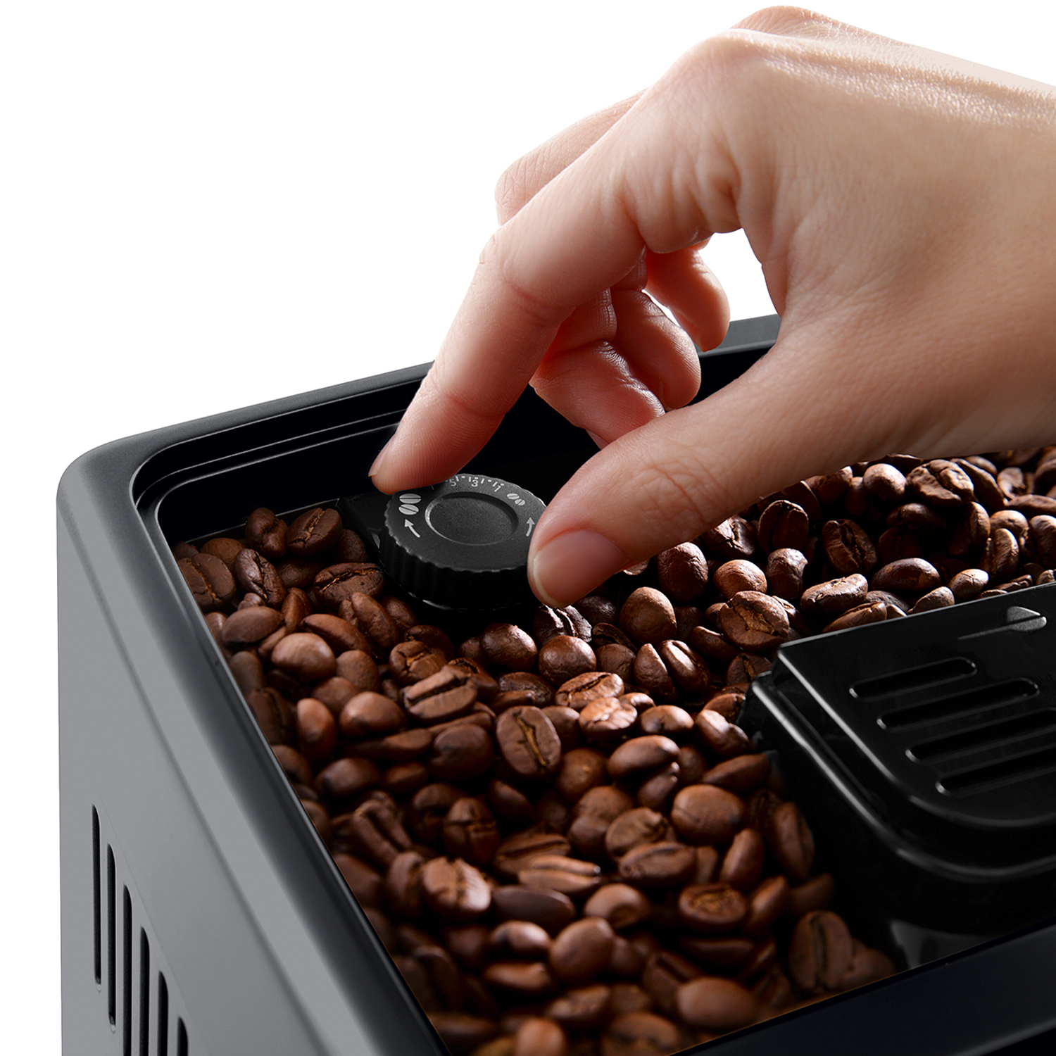 Un primo piano di chicchi di caffè all'interno di una macchina per il caffè, una mano regola la macinatura.