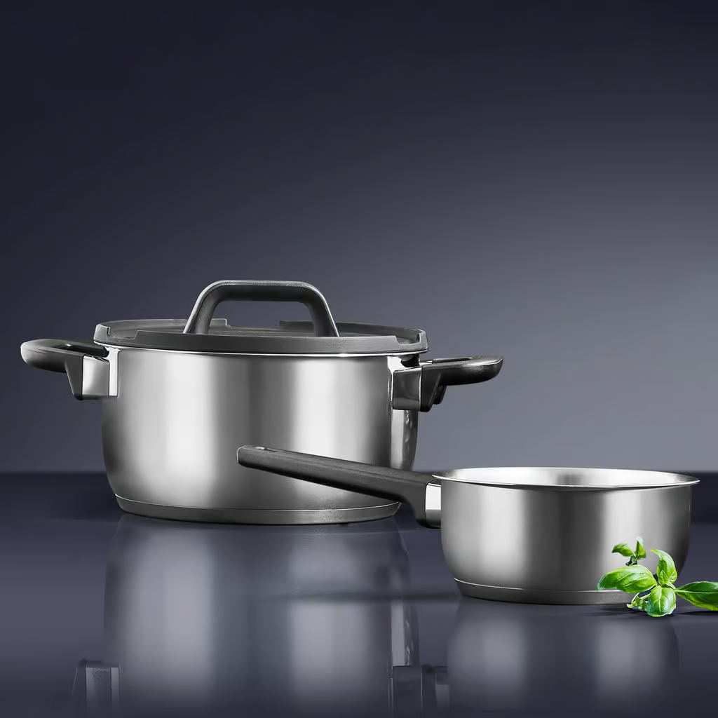 Zestaw garnków ze stali nierdzewnej i mała patelnia na odblaskowej powierzchni.