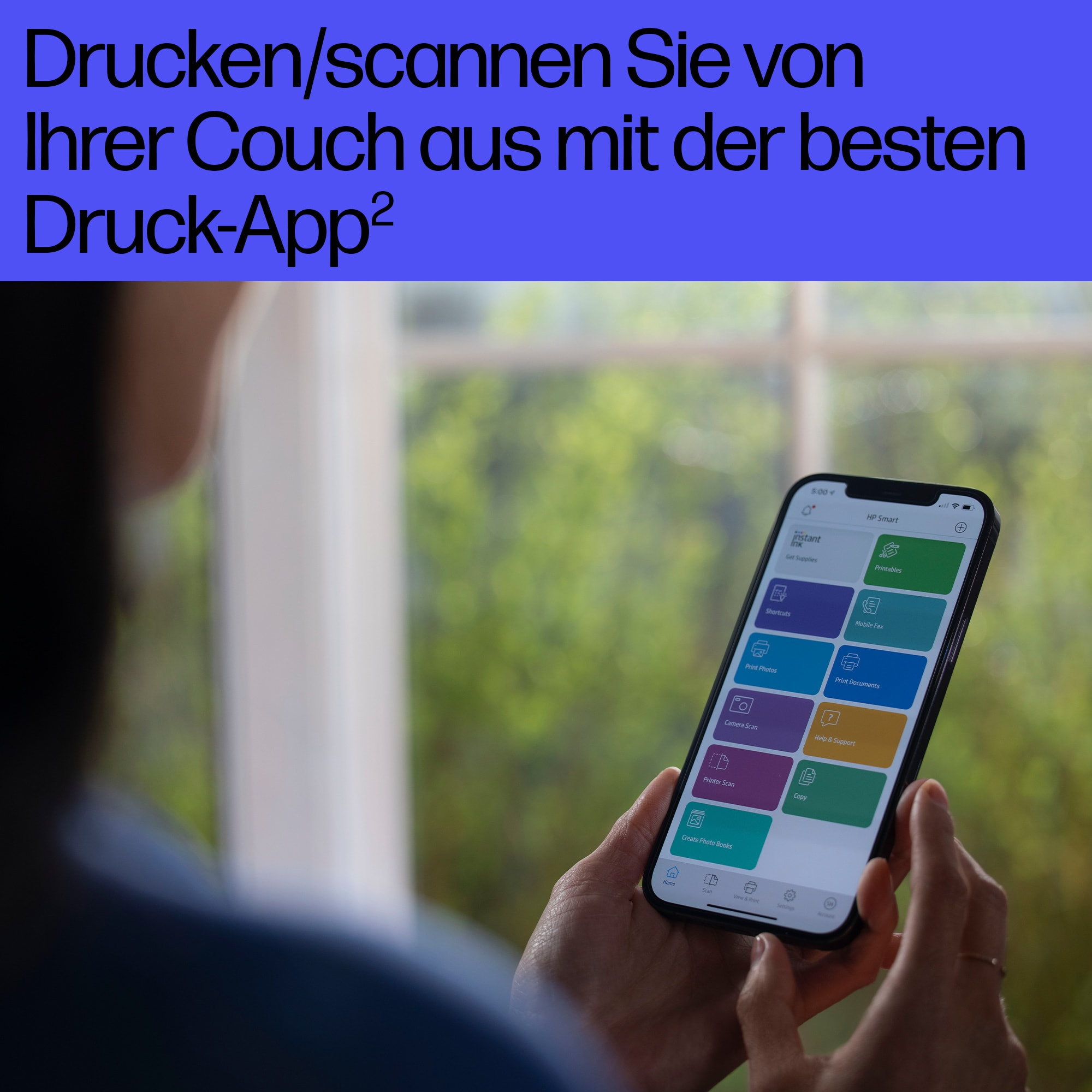 Person hält ein Telefon mit geöffneter App. Text: Drucken/scannen Sie von Ihrer Couch aus mit der besten Druck-App².