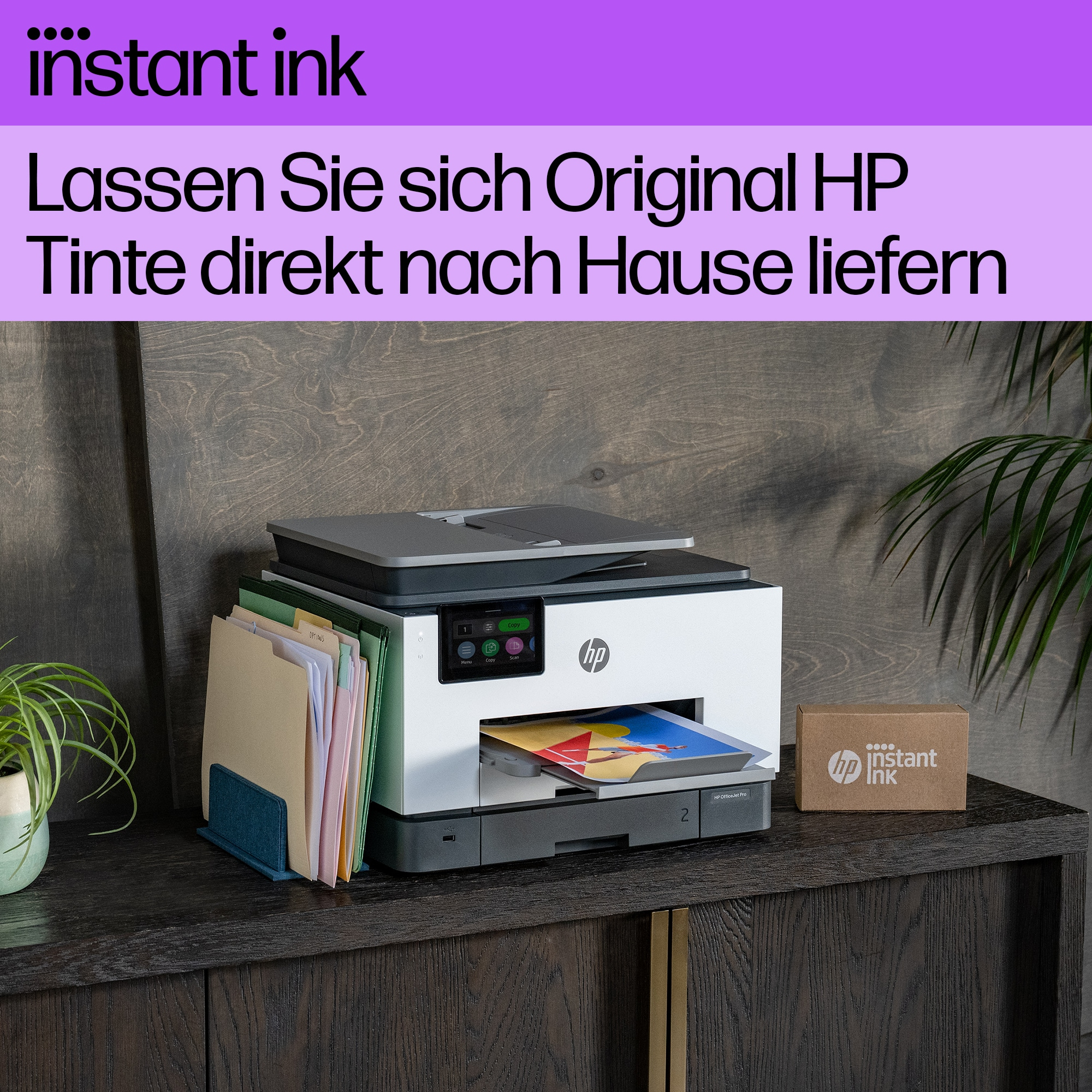 Ein weißer und grauer HP-Drucker auf einem Holzschrank, daneben eine Pflanze und Akten.