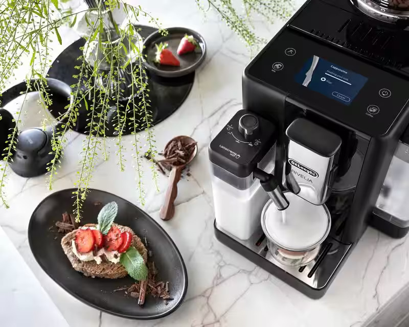 Ekspres do kawy z jedzeniem, talerz tostów z truskawkami i wiórkami czekoladowymi.