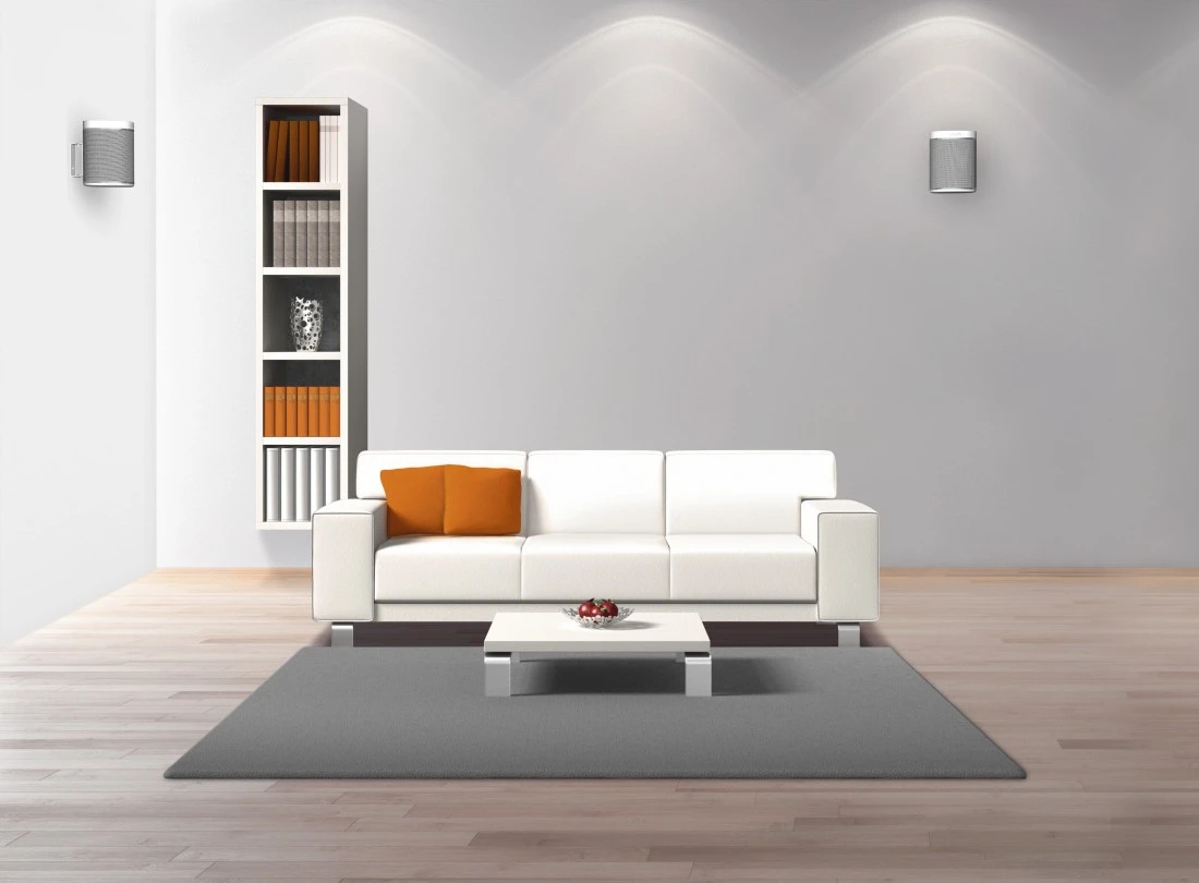 Wohnzimmer mit weißem Sofa, orangefarbenem Kissen, grauem Teppich, Couchtisch, Bücherregal und Wandlautsprechern.