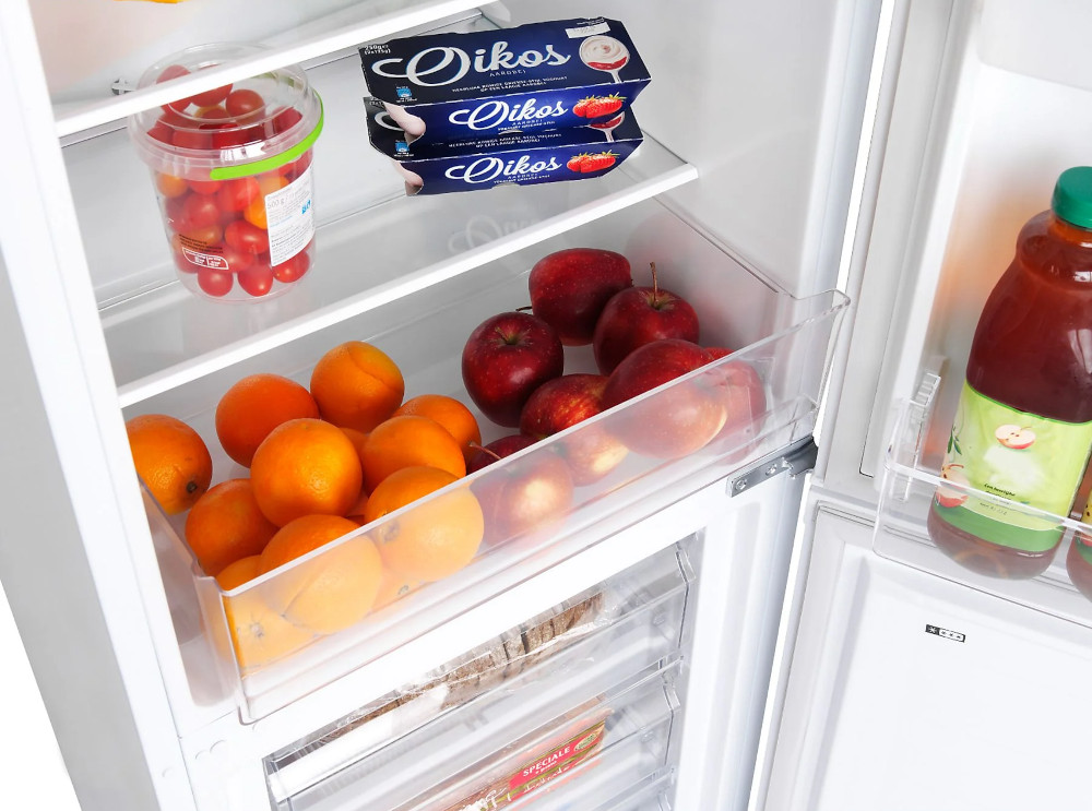 Inside of a refrigerator, with fruits and yogurt visible on the shelves. White background.