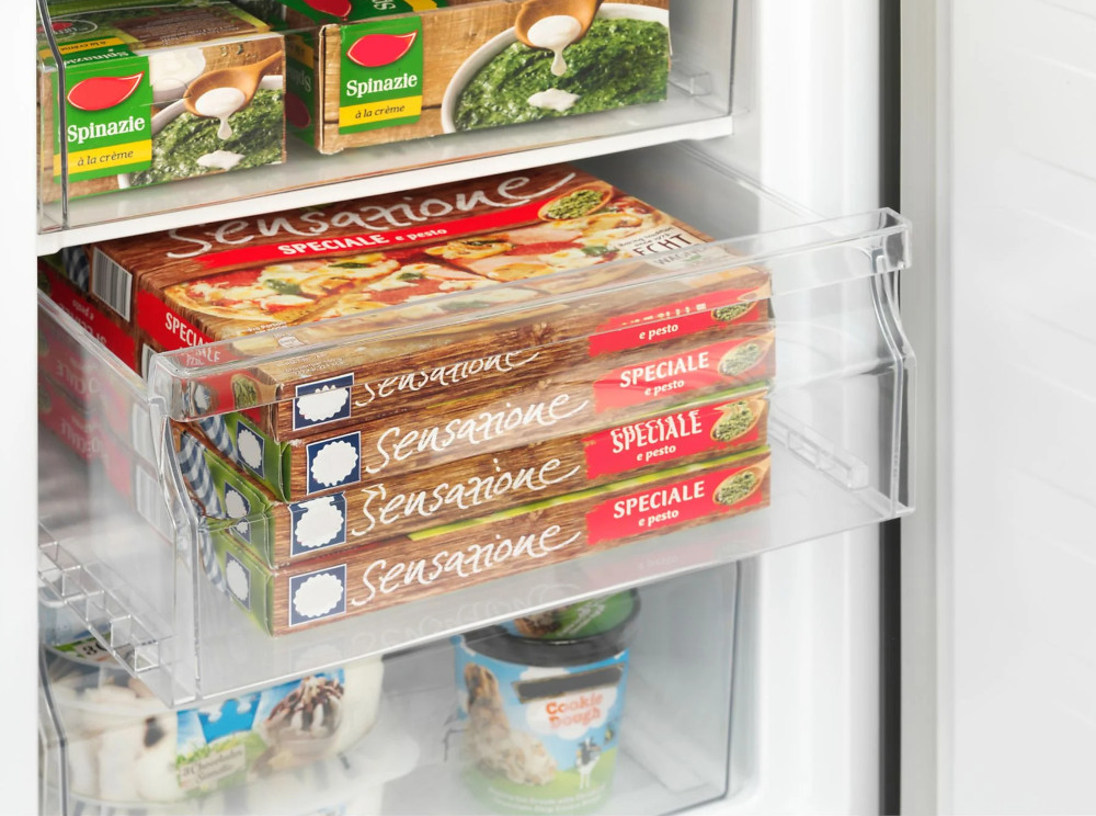 Un réfrigérateur rempli d'aliments surgelés, y compris des pizzas et des boîtes d'épinards.