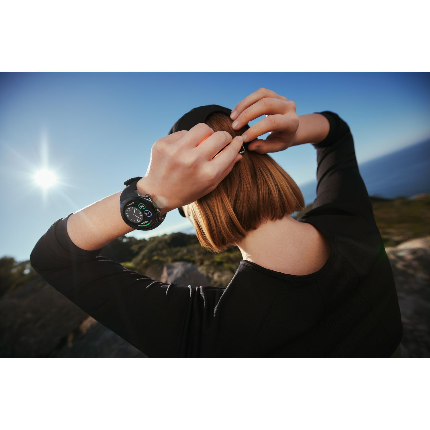 Une personne ajuste une montre intelligente à son poignet. Ciel bleu en arrière-plan.