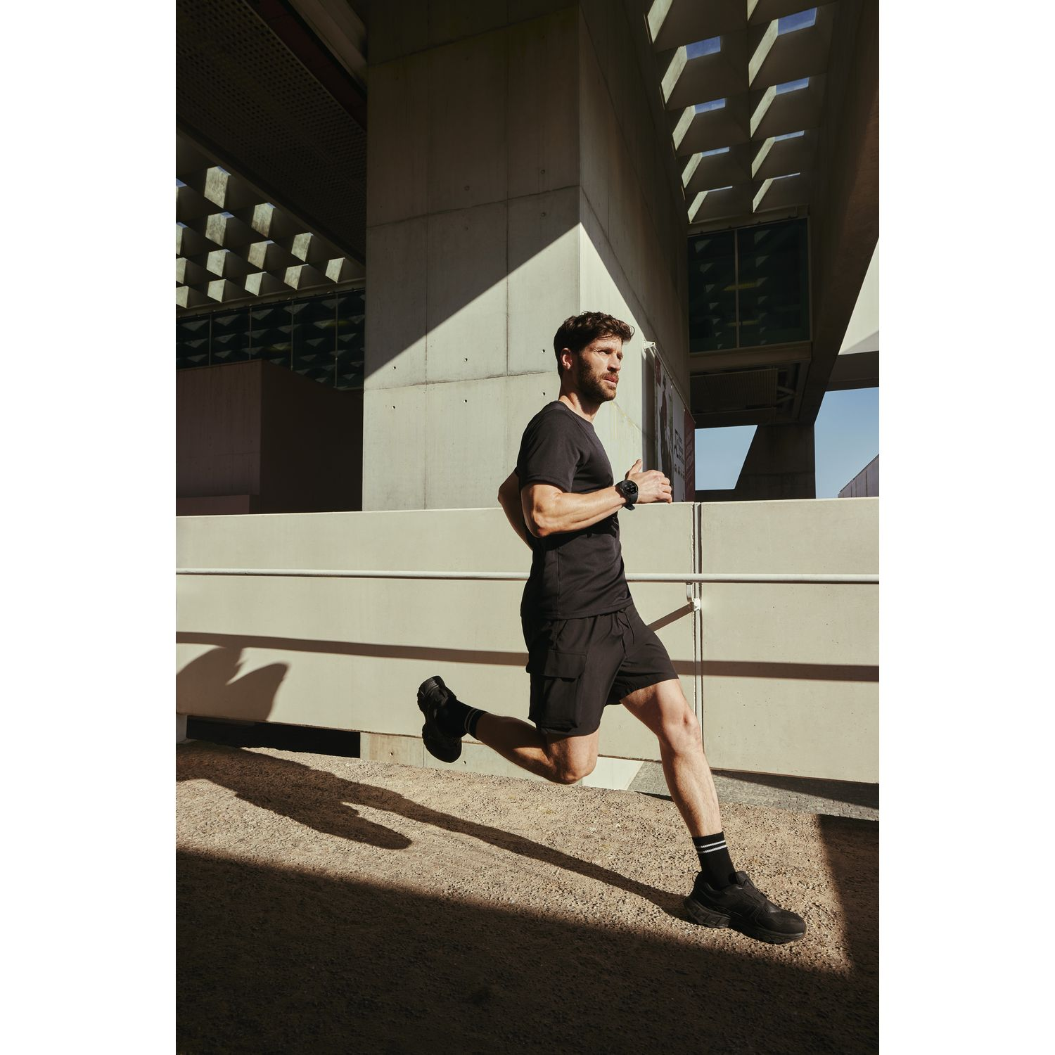 Un homme courant dans un cadre extérieur ensoleillé. Il porte un short noir et un t-shirt. L'arrière-plan est flou.