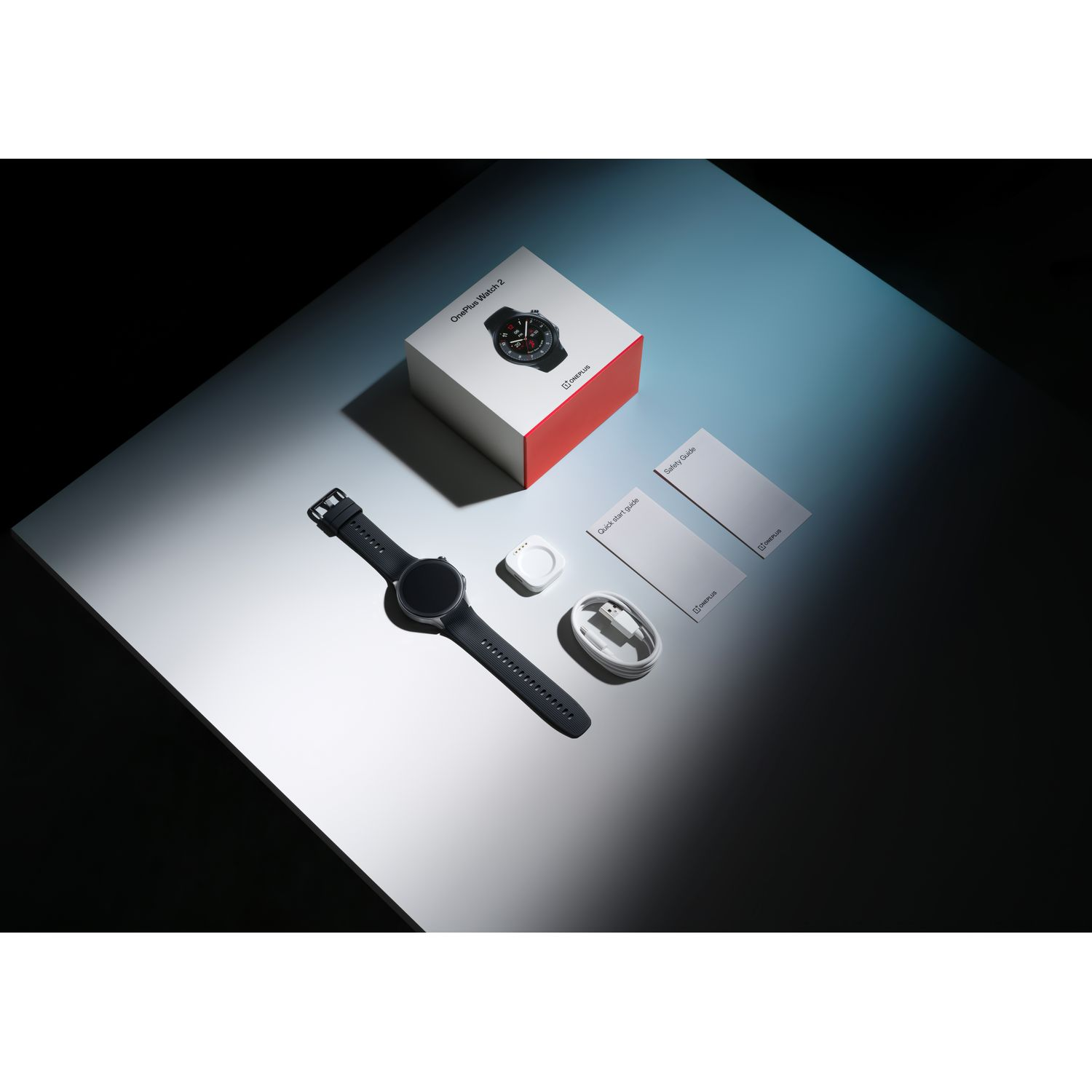 Une smartwatch et des accessoires sont disposés sur une surface réfléchissante, dont une boîte, un chargeur et des documents.
