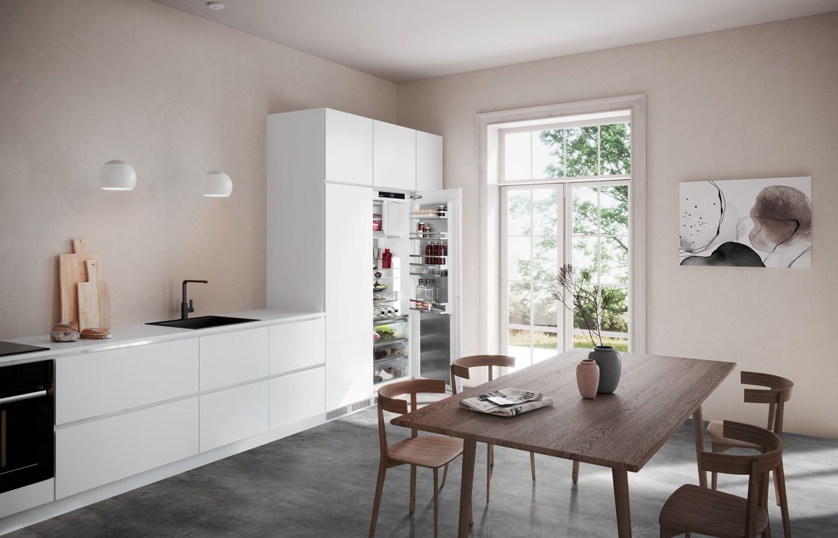 Weiße Küche mit offenem Kühlschrank, Holztisch und Fenster mit Bäumen.