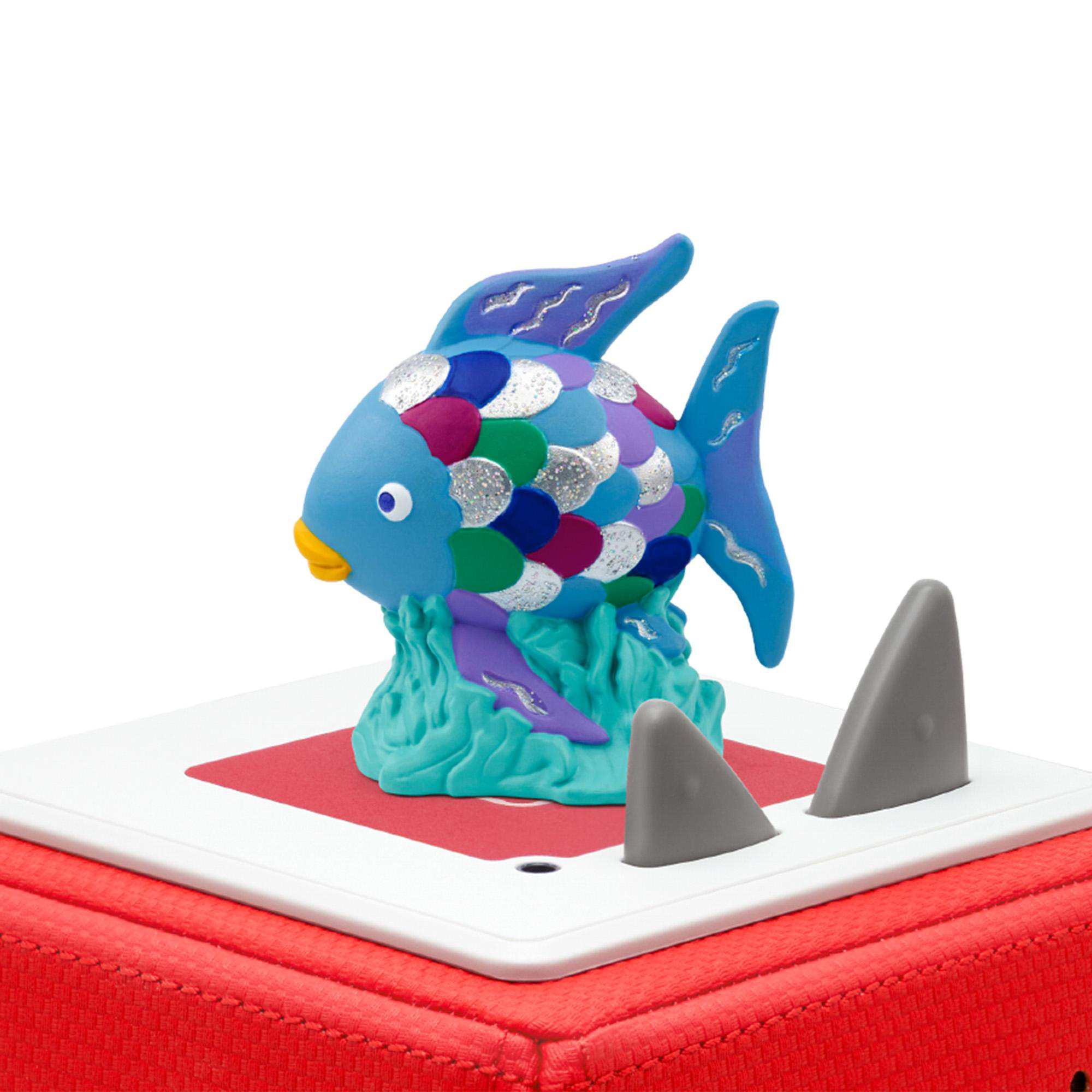 Ein farbenfrohes Fischspielzeug auf roter Oberfläche, mit zwei grauen Haifischflossen. Blaue, lila und silberne Schuppen.