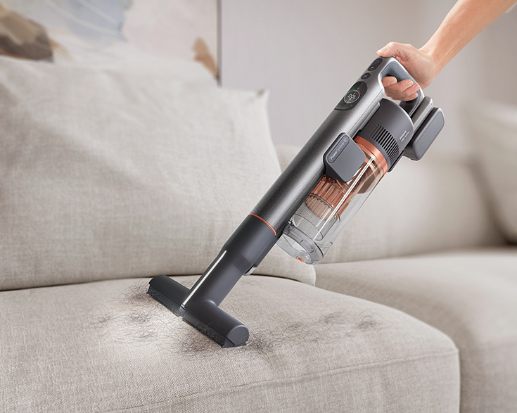 Kéz porszívót használ a kanapén. Haj a kanapén. Homályos háttér.