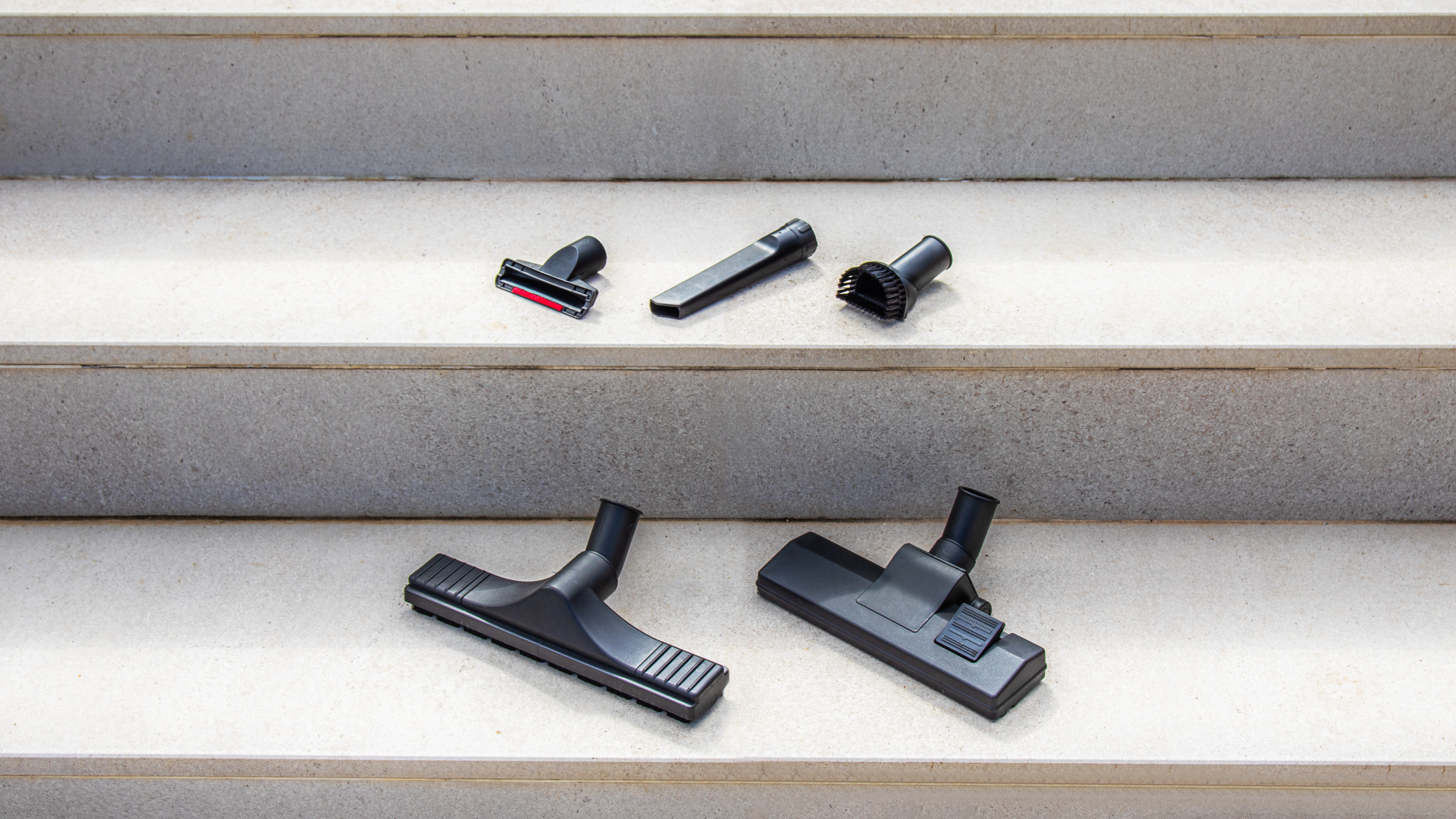 Accesorios de aspiradora colocados en escalones. Fondo blanco.