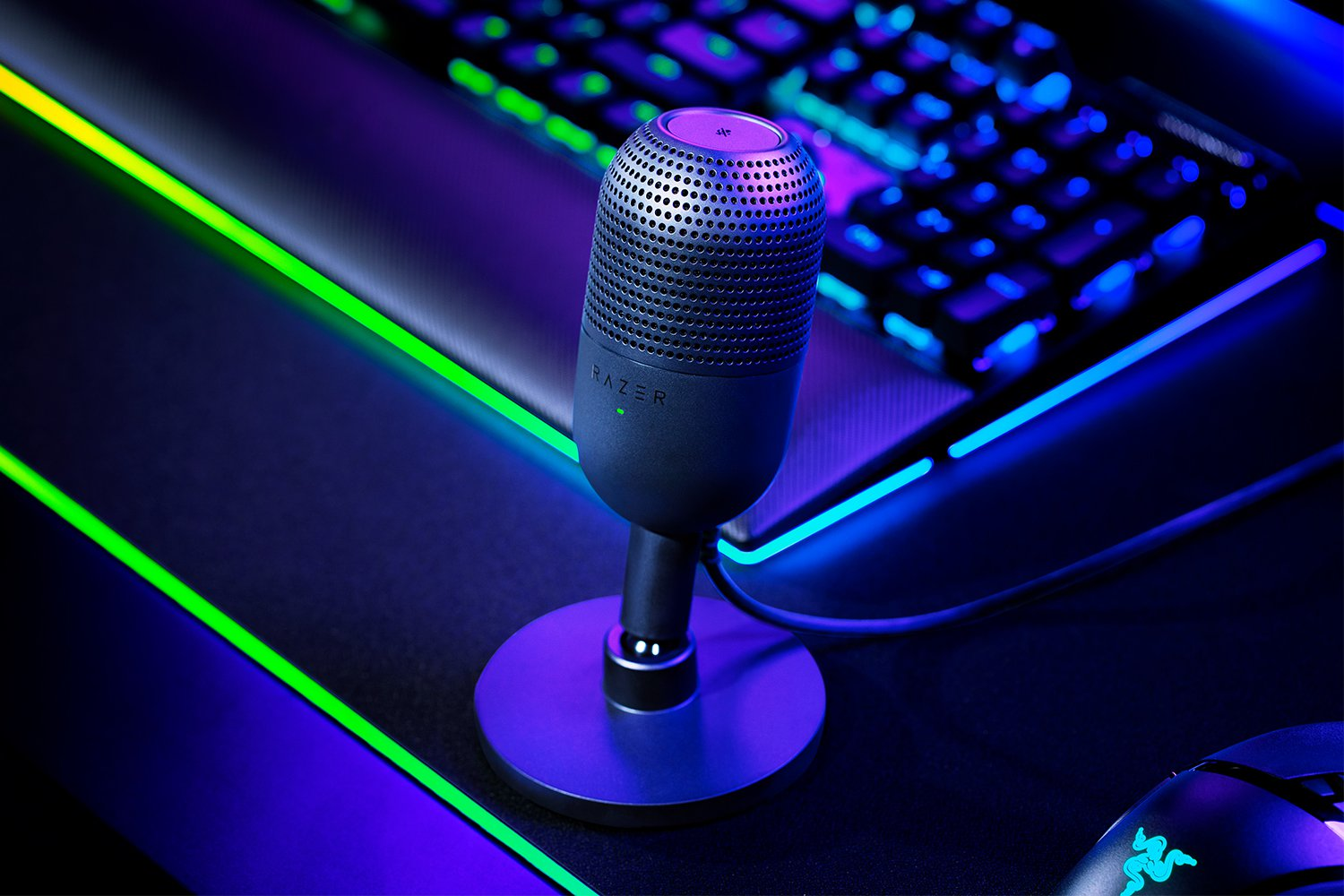 Ein Razer-Mikrofon auf einem Schreibtisch mit Tastatur und Maus, beleuchtet mit blauen und grünen Lichtern.