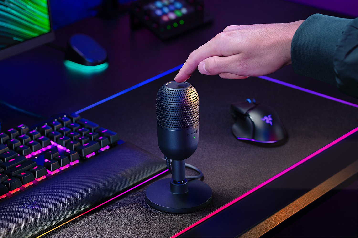 Ein schwarzes Razer-Mikrofon auf einem Schreibtisch. Der Finger einer Person drückt auf eine Taste.