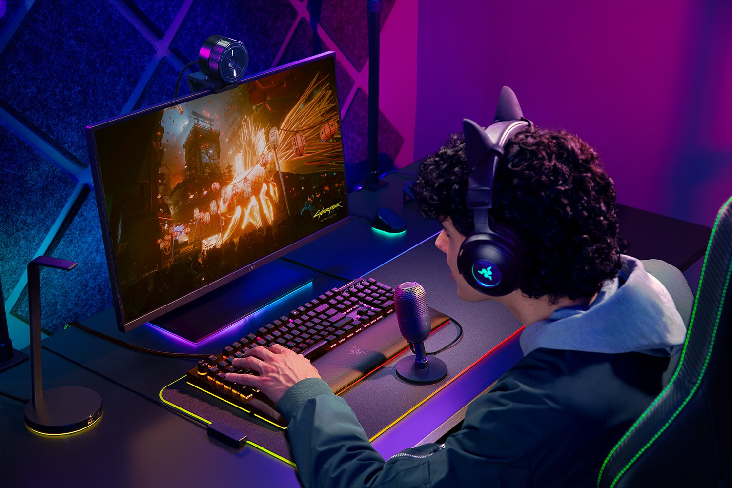 Ein Gamer mit Katzenohrkopfhörern und Mikrofon spielt ein Spiel auf einem Computer mit bunten Lichtern.