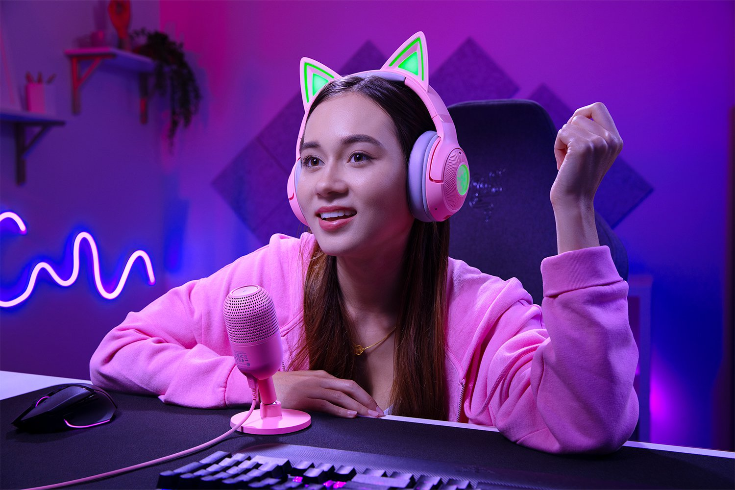 Una donna con cuffie rosa con orecchie da gatto e un microfono, sorride mentre gioca.
