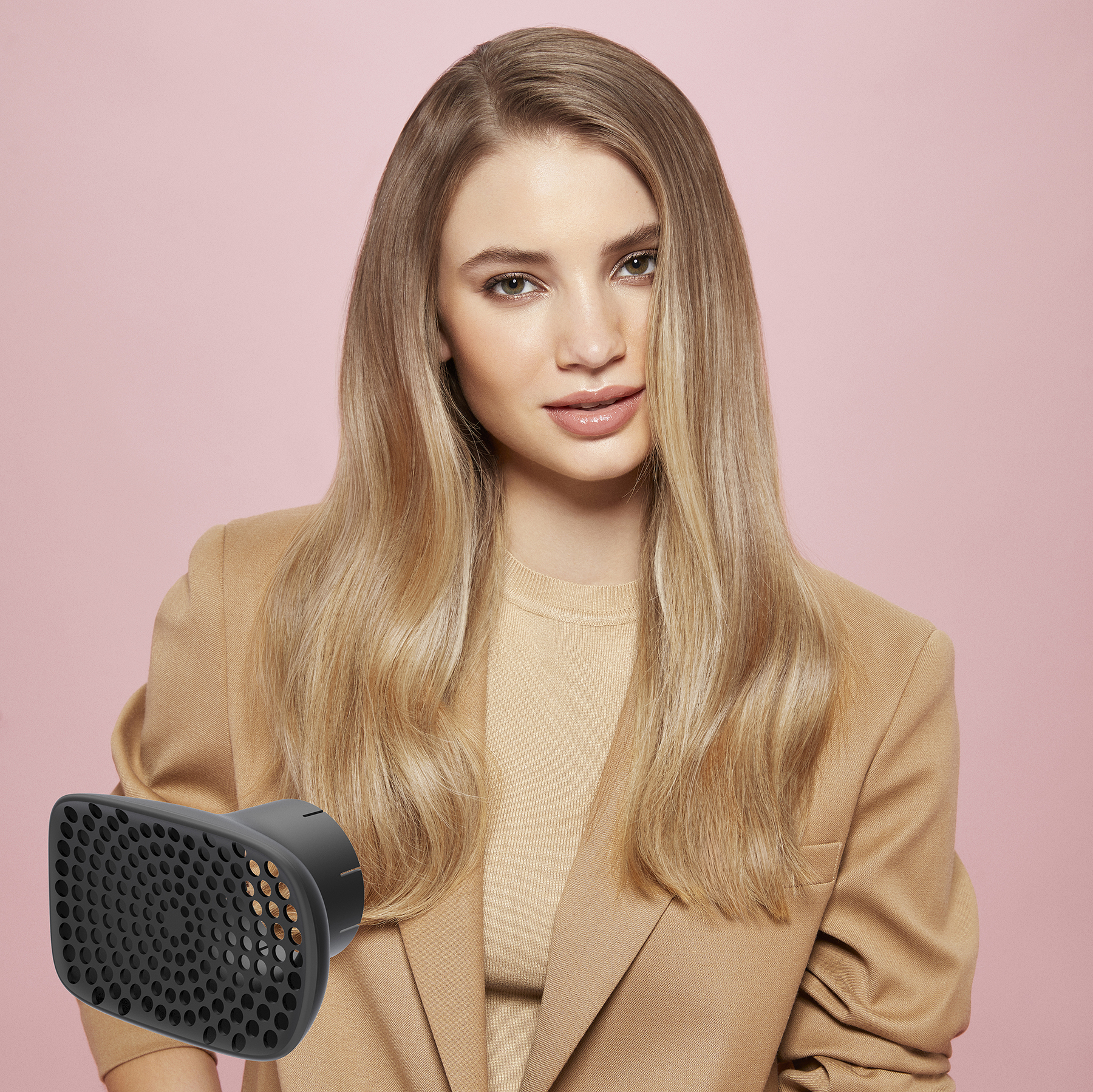 Femme blonde avec cheveux et un diffuseur noir devant un fond rose.