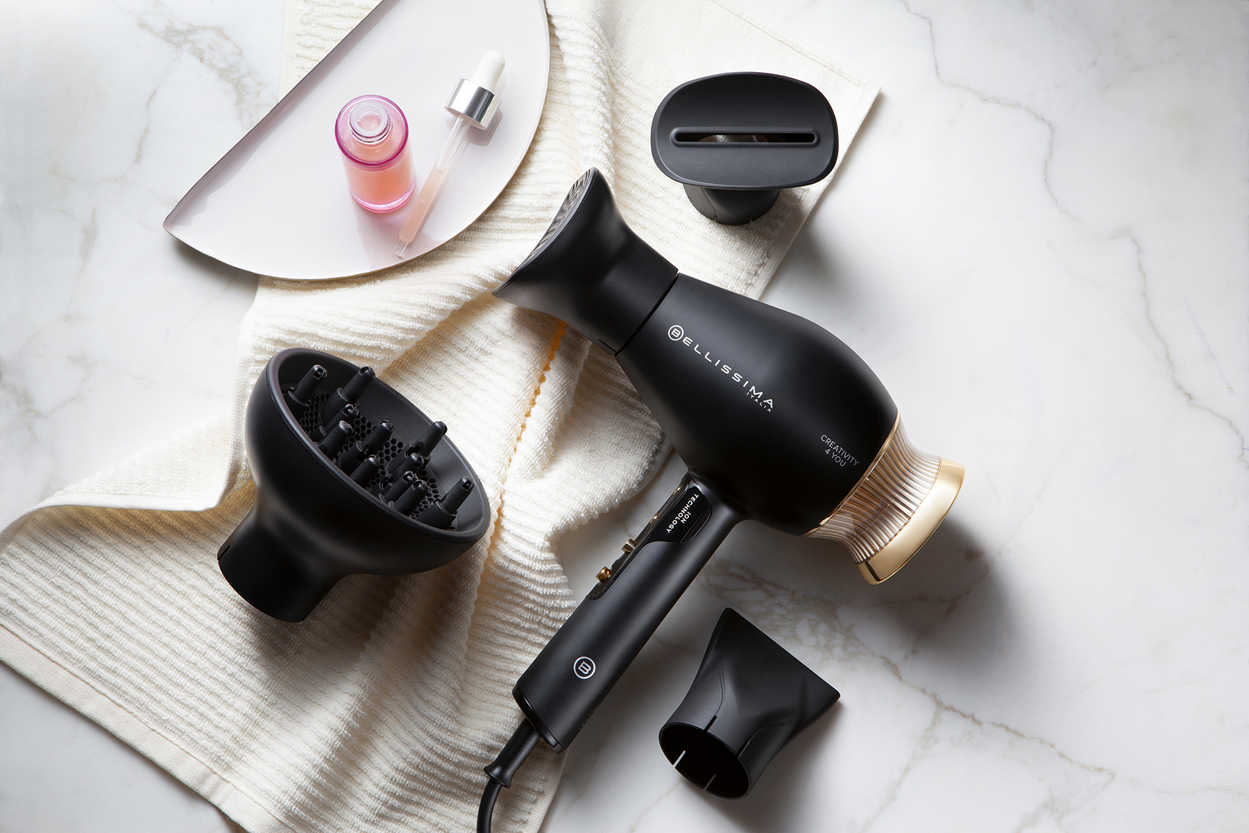 Sèche-cheveux noir avec accessoires, un plateau avec des produits, sur une surface en marbre.