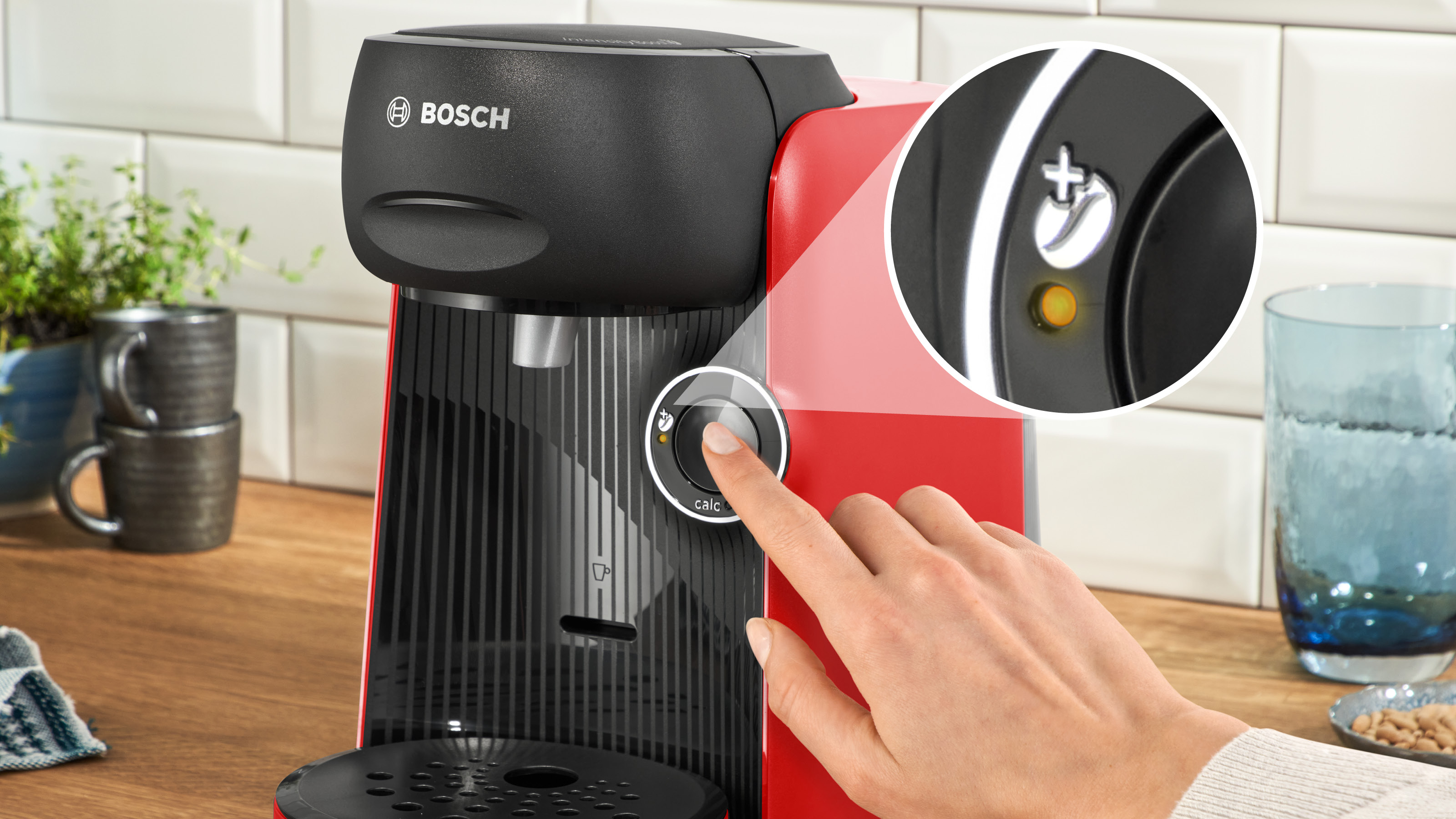 Nahaufnahme einer roten Kaffeemaschine, wobei eine Hand einen Knopf drückt. Kreis mit Text 'calc' betont.