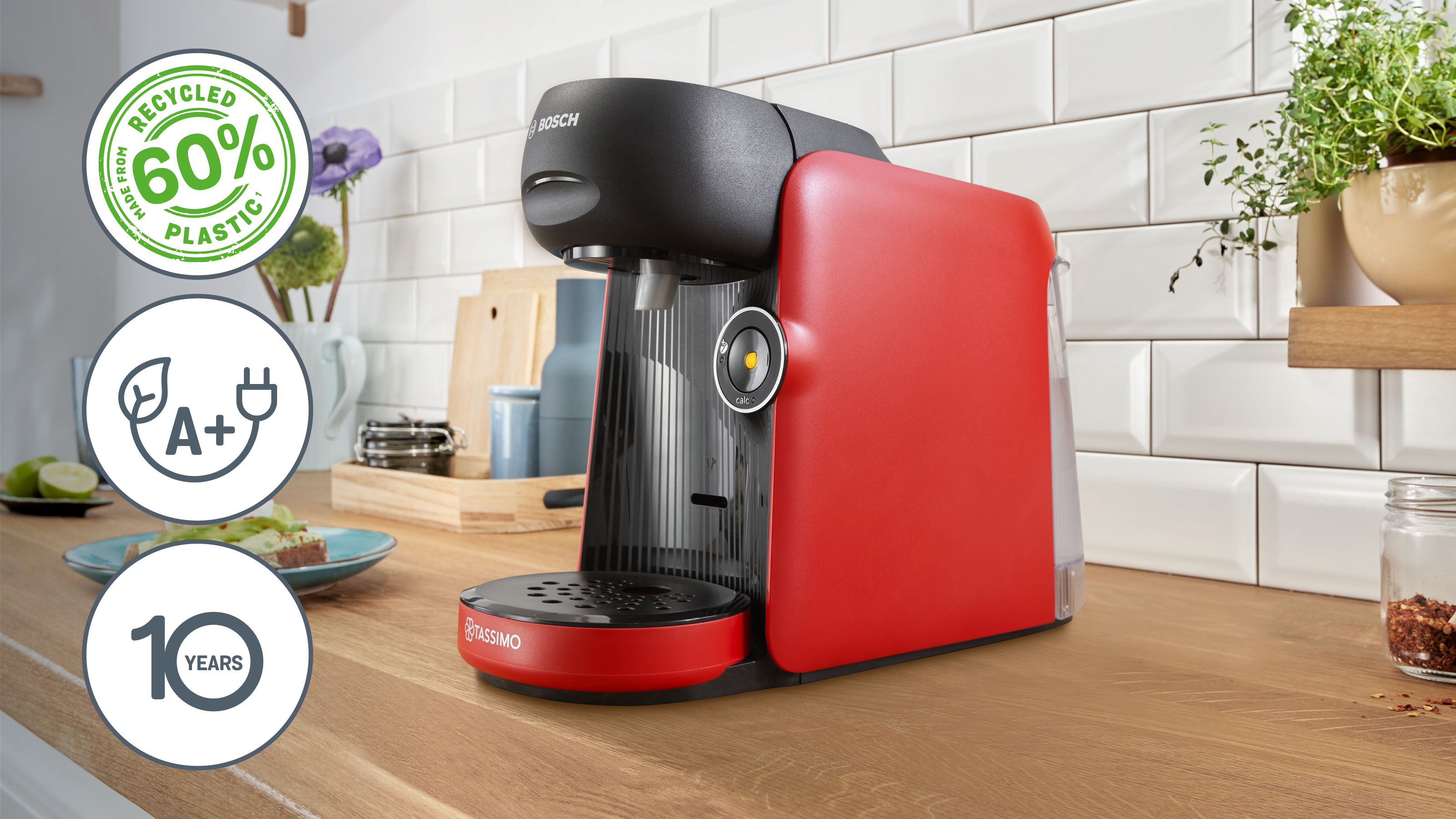 Rote Tassimo Kaffeemaschine auf Holztheke mit Öko-Symbolen und Blick in eine Küche.
