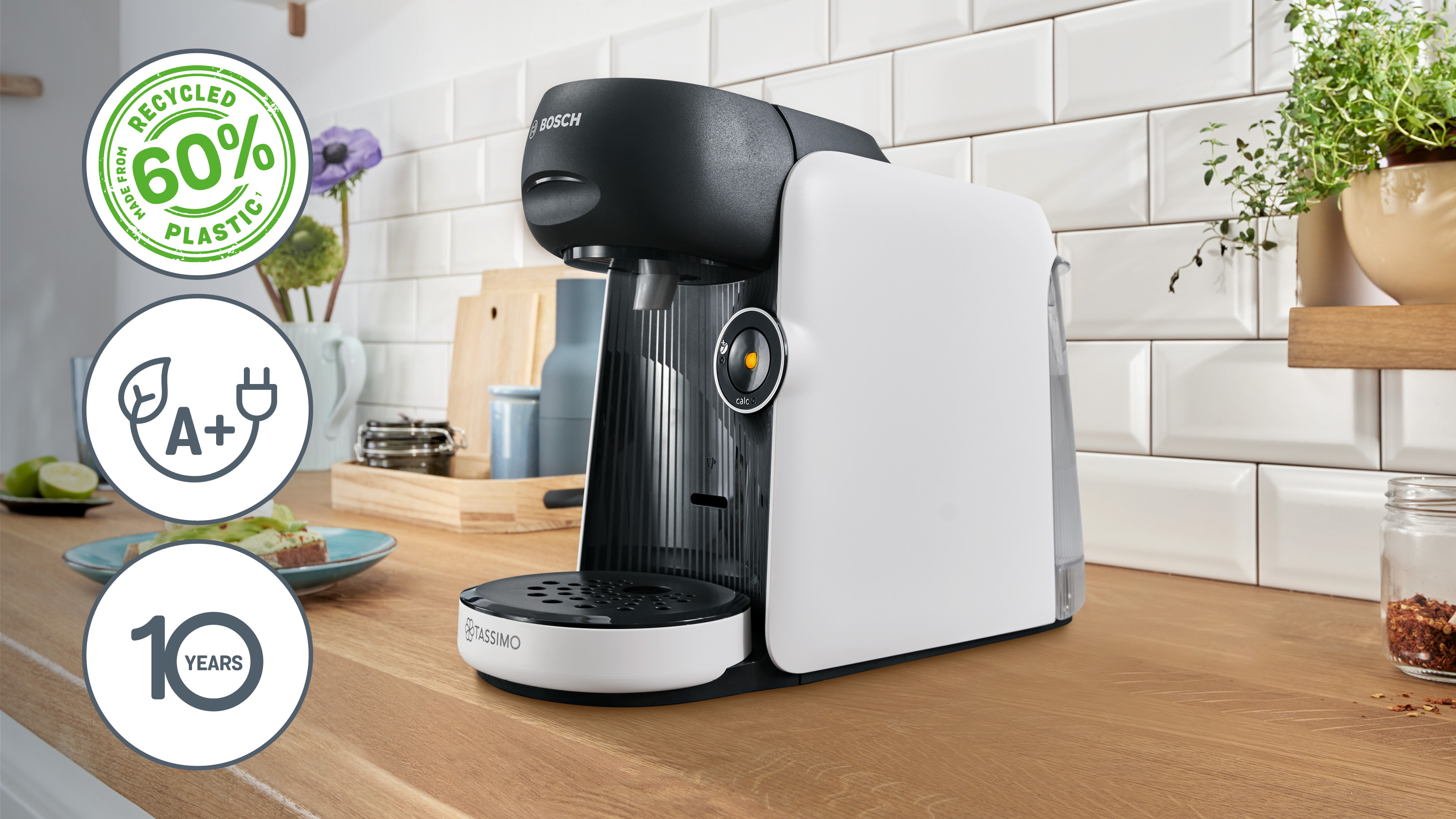 Bosch Tassimo Kaffeemaschine auf einer Holztheke, mit Recycling- und Energieeffizienz-Symbolen.