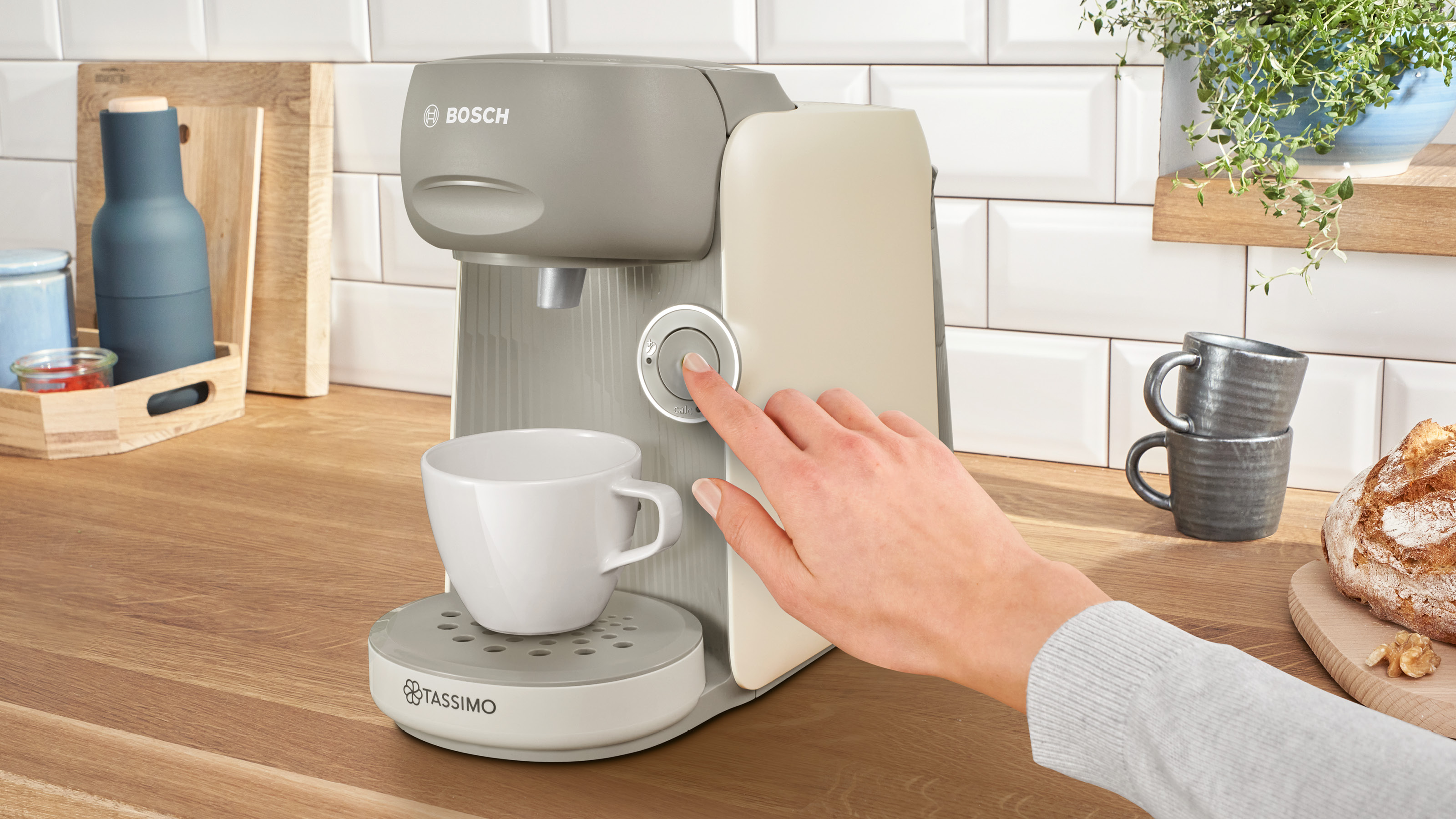 Die Hand einer Person drückt die Taste an einer Bosch Tassimo Kaffeemaschine.