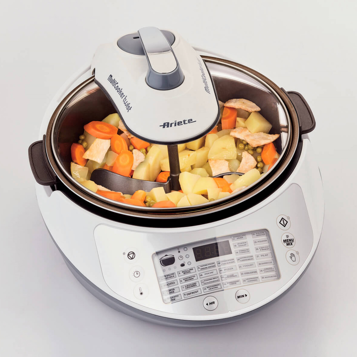 Multicooker bianco con verdure. Ha un coperchio con manico e display digitale.