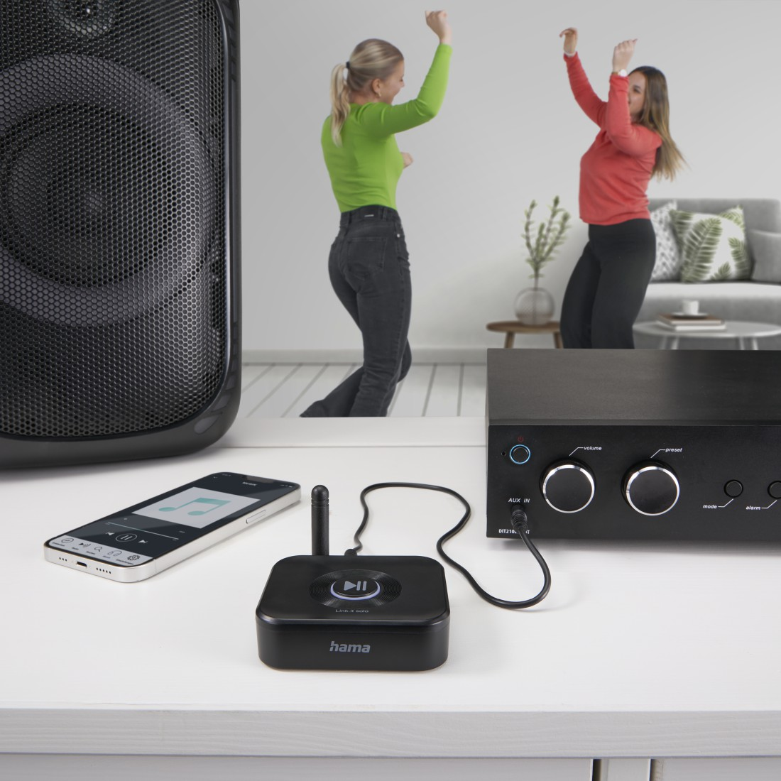 Tanzende Personen in der Nähe von Lautsprecher und Soundsystem. Telefon und Hama-Gerät auf dem Tisch.