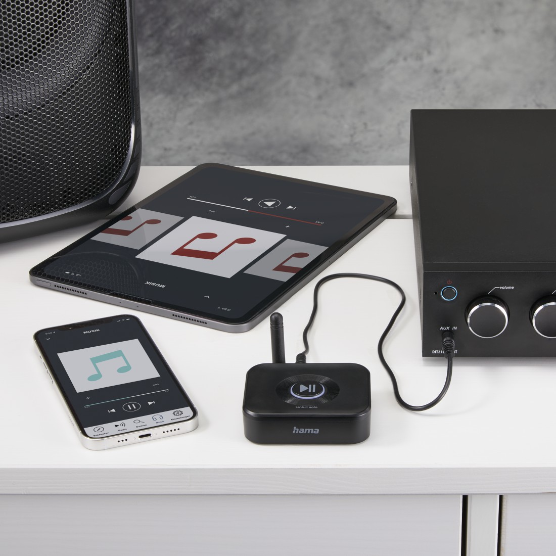 Ein Musik-Setup mit Tablet und Telefon, einem schwarzen Empfänger und Lautsprecher. Weiße Oberfläche.