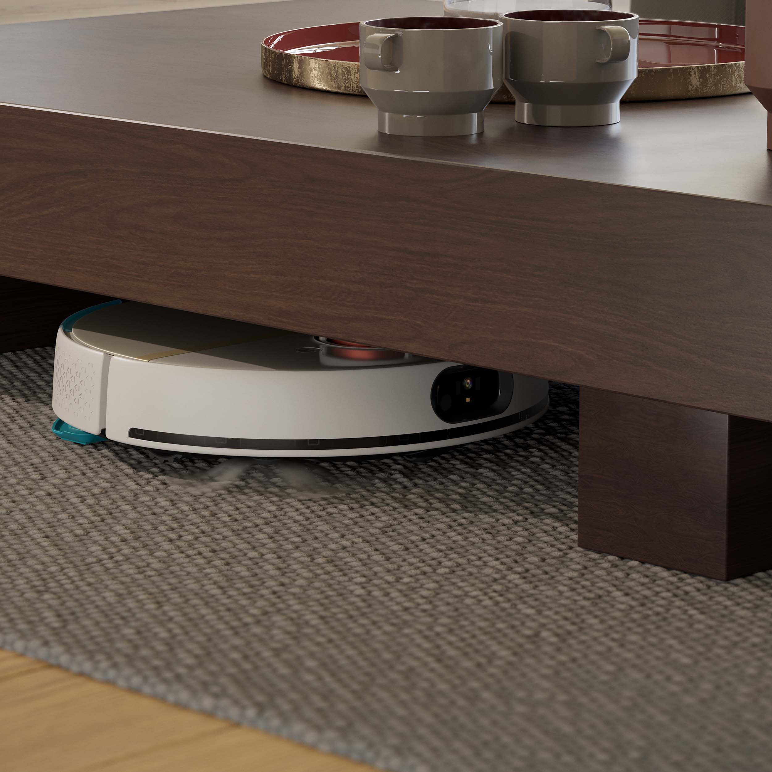 Robot sprzątający pod ciemnobrązowym stolikiem na szarej wykładzinie. Dwie filiżanki na stole.