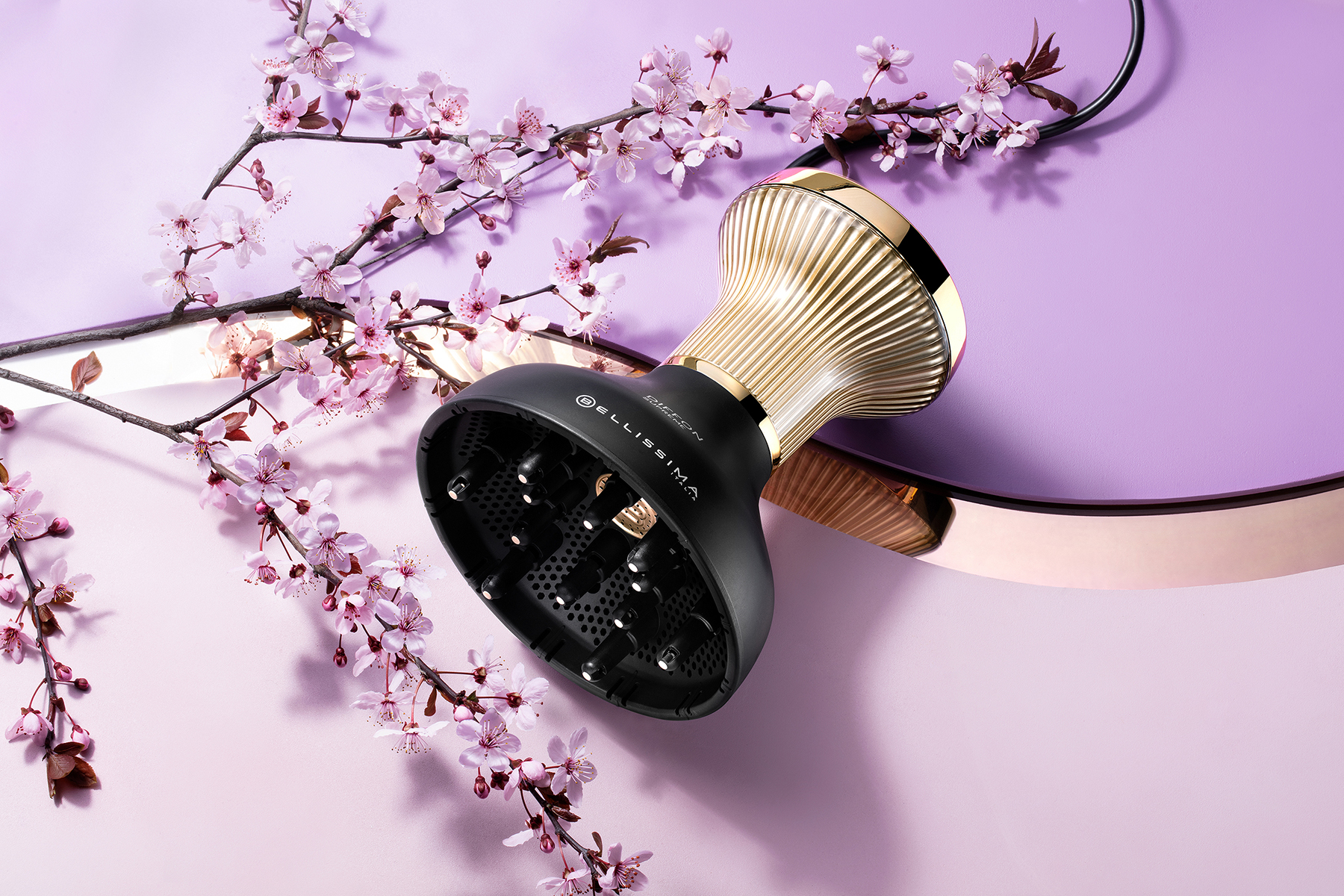 Un diffuseur de cheveux noir et doré avec des branches de fleurs de cerisier sur un fond violet.