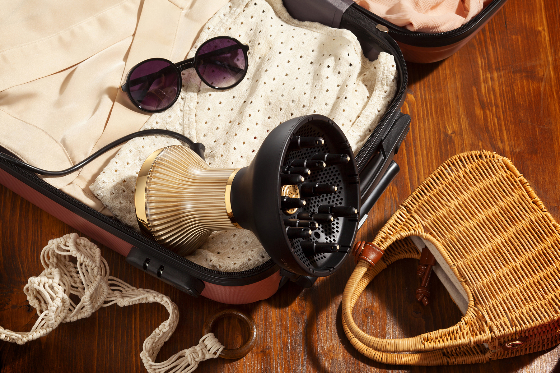 Valise ouverte, avec lunettes de soleil, sèche-cheveux, vêtements et un petit sac sur une surface en bois.