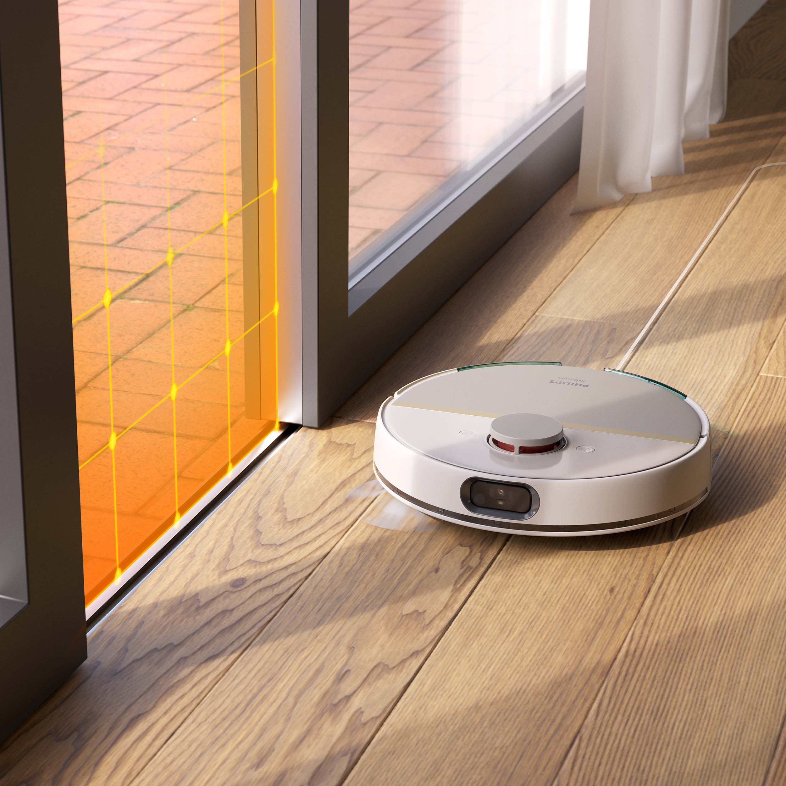Biały robot odkurzający na drewnianej podłodze, w pobliżu szklanych drzwi z pomarańczowym wzorem kratki.