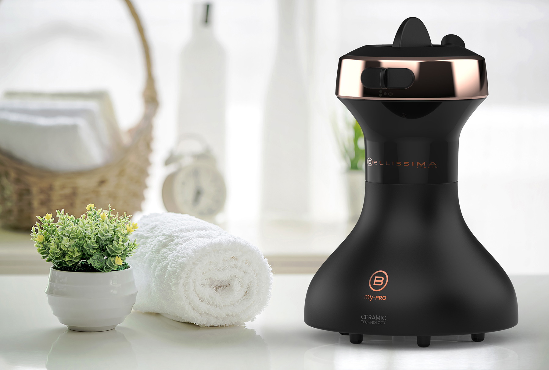 Un sèche-cheveux noir et cuivré avec une serviette blanche et une plante en arrière-plan sur une table blanche.