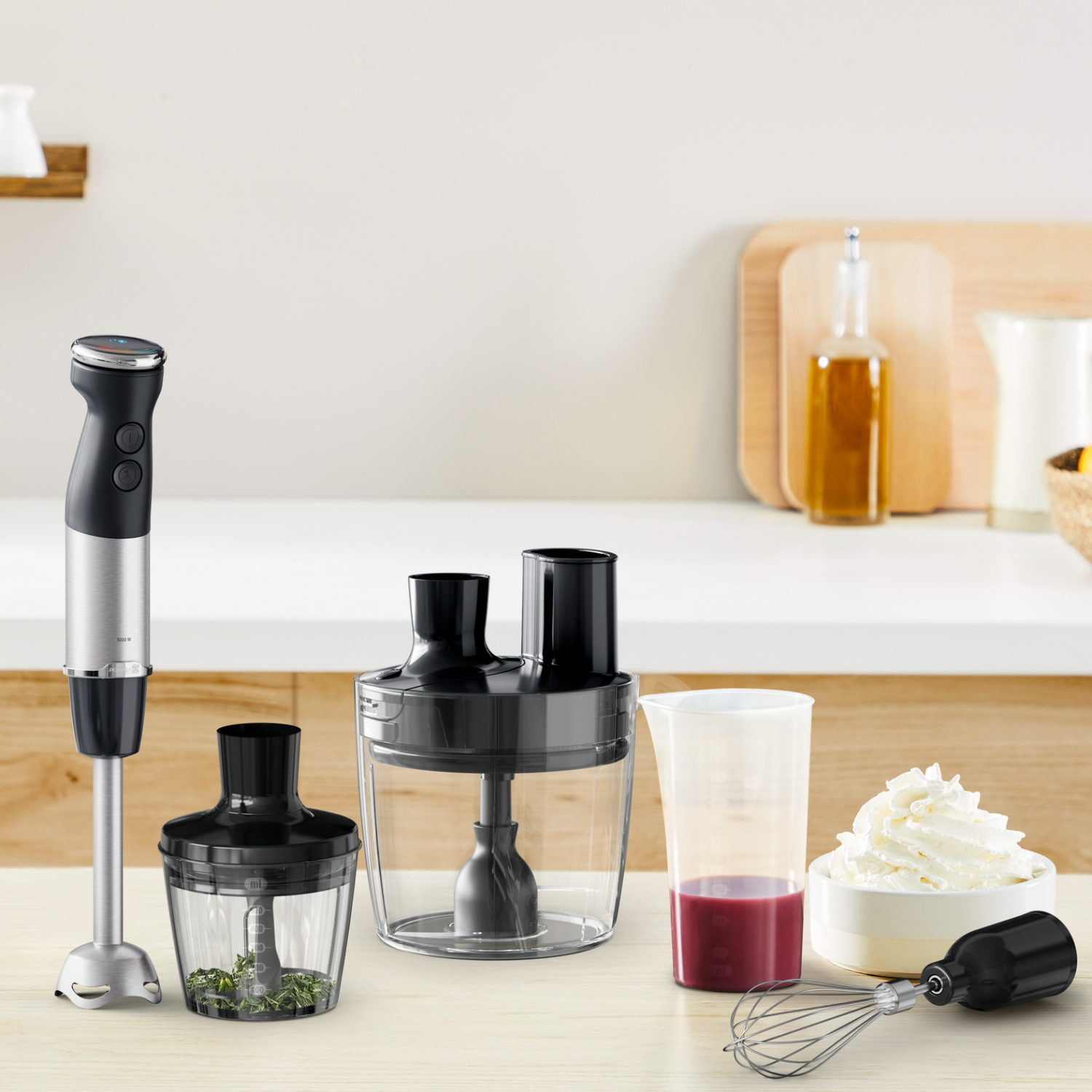 Blender and accessories on a table. Includes a hand blender, containers, and a whisk.