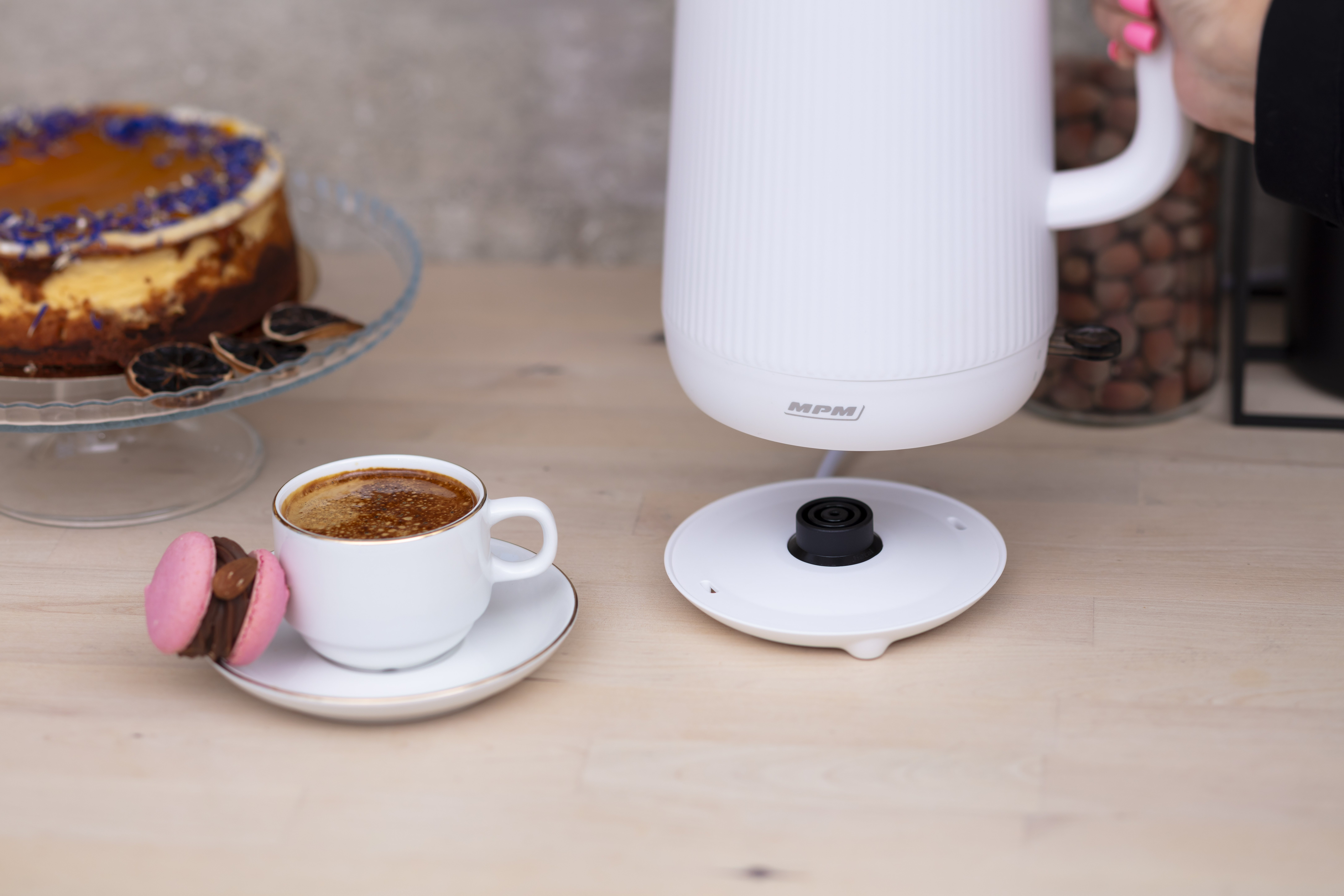 Filiżanka kawy i makaronik obok białego czajnika.